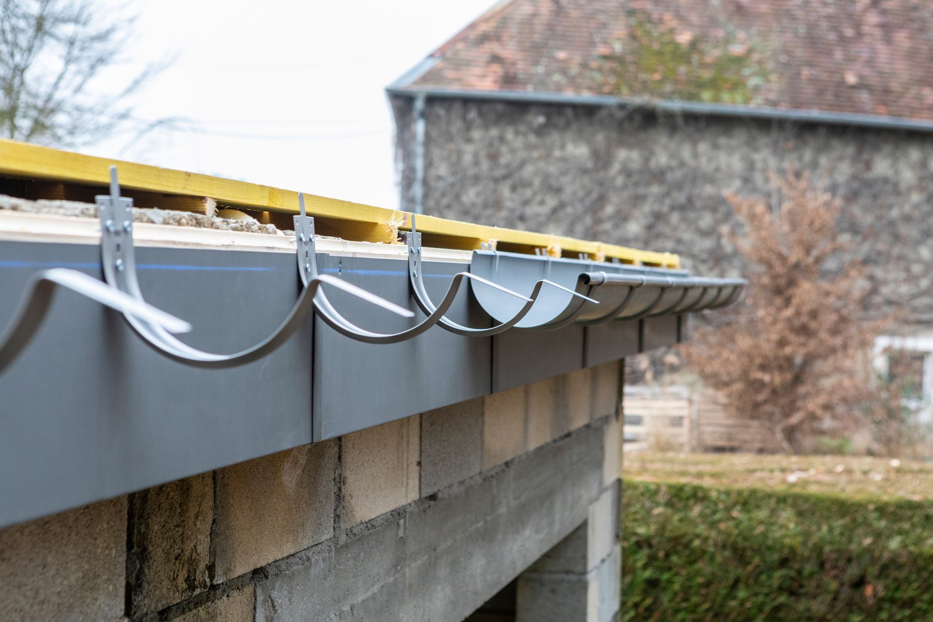 Une rangée de supports de gouttière métalliques fixés au bord d'un toit au-dessus d'un mur en parpaings.