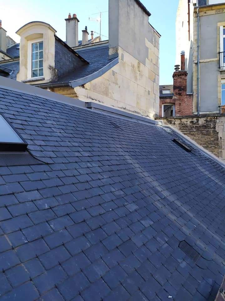 Vue par-dessus un toit de tuiles brunes en direction d'un bâtiment voisin et d'une cheminée en briques au coucher du soleil.