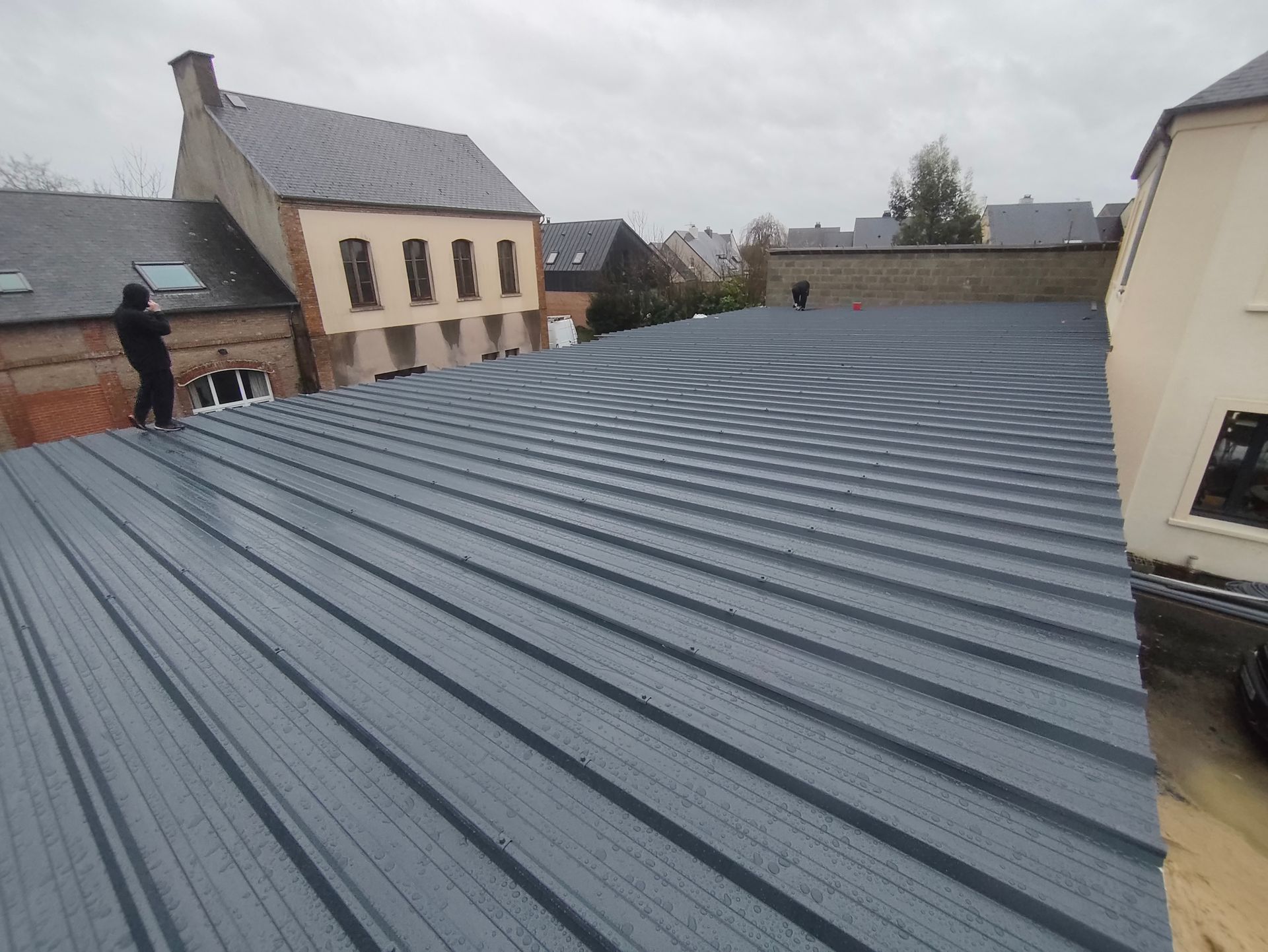 Vue aérienne de plusieurs toits de tuiles, l'un montrant des chevrons en bois apparents en construction, d'autres avec des tuiles en terre cuite.