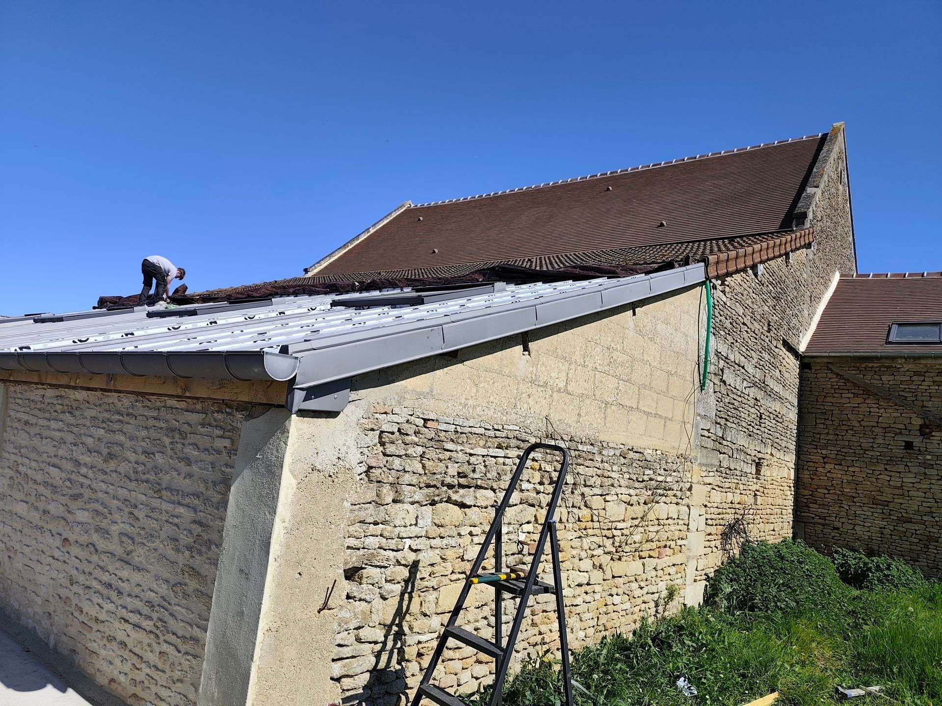 Gros plan sur un toit métallique à joints debout et une flèche décorative se détachant sur un ciel bleu vif parsemé de nuages ​​épars.