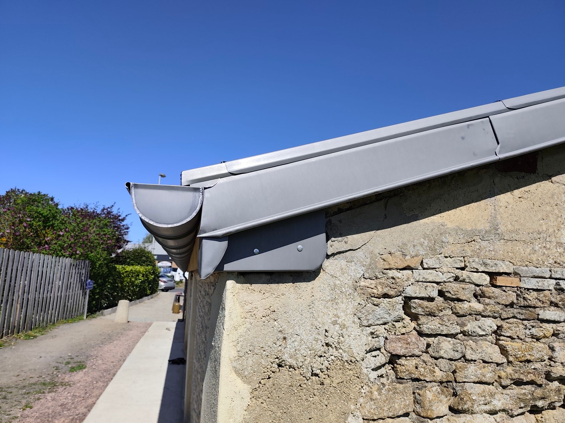 Vue en contre-plongée d'une gouttière et d'une descente pluviale en métal gris fixées à un bâtiment avec un mur et un soffite en stuc beige.
