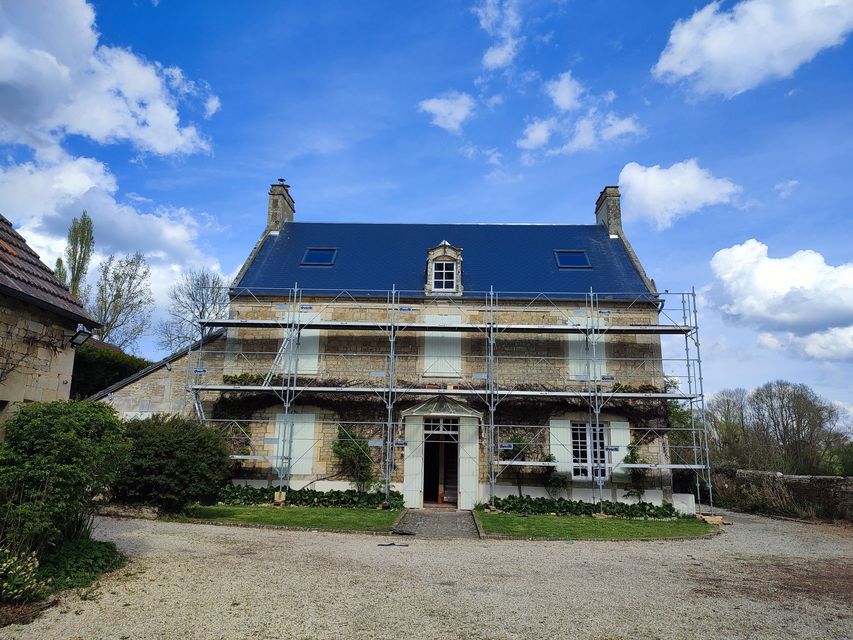 Vue en contre-plongée de tuiles de toit en terre cuite se détachant sur un ciel bleu parsemé de nuages ​​épars.
