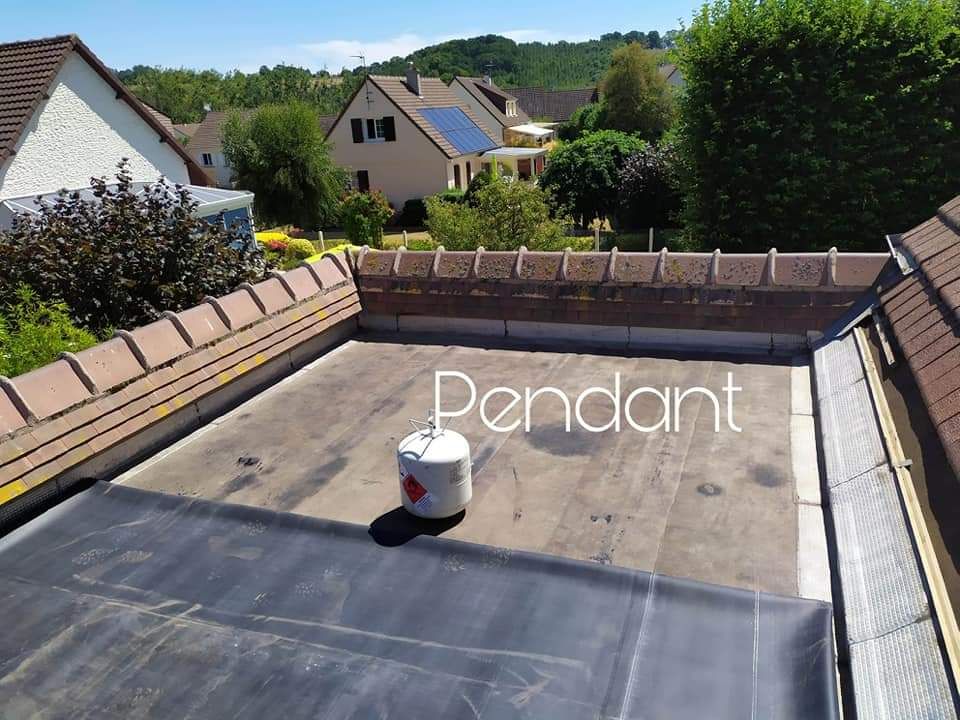 Un ouvrier du bâtiment utilise un pistolet thermique pour sceller un rouleau de membrane de toiture noire sur une terrasse en panneaux OSB.
