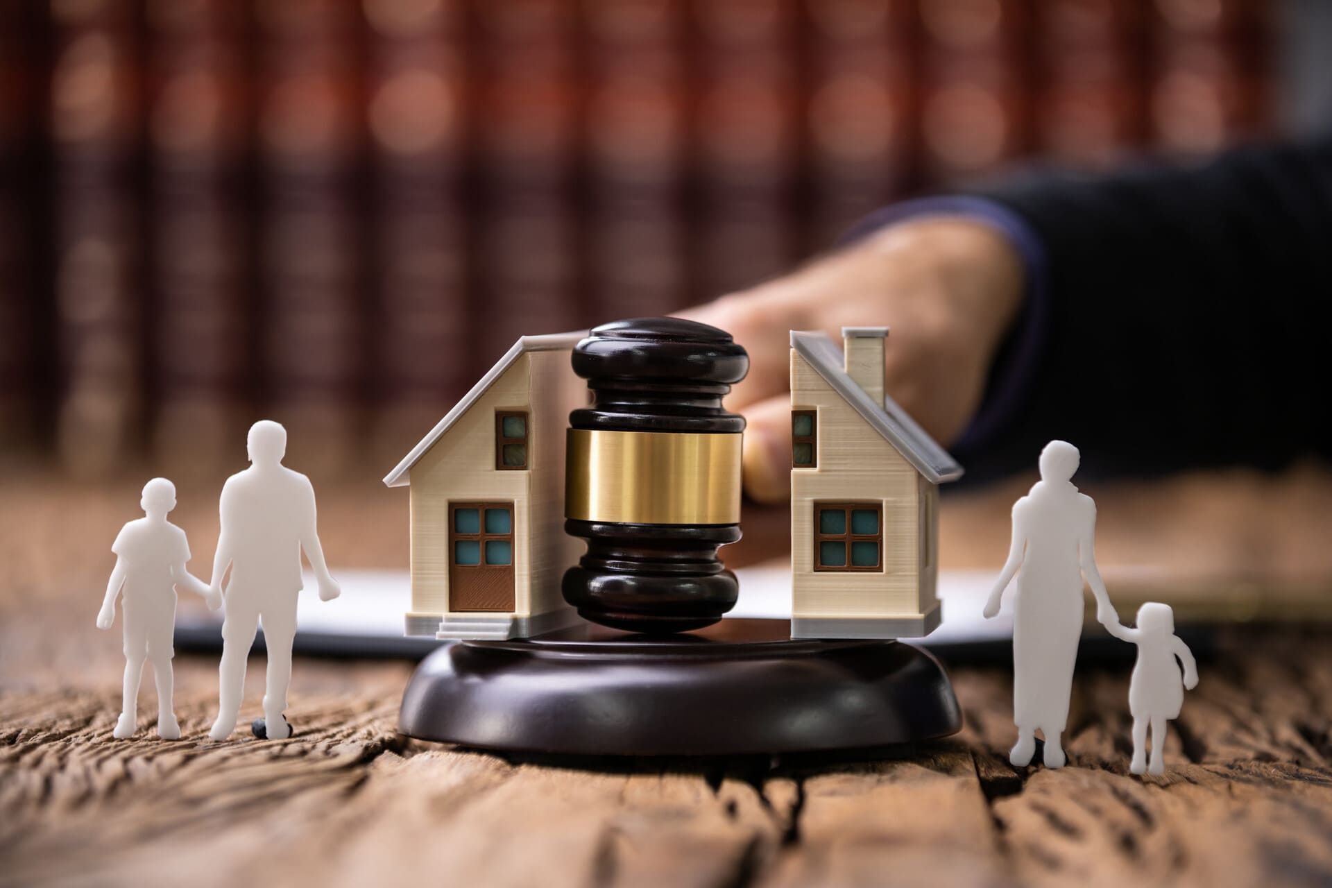 Mazo frente a una maqueta de una casa con un escritorio de juez y pequeñas figuras, que simbolizan la ejecución hipotecaria de una vivienda o una disputa legal.