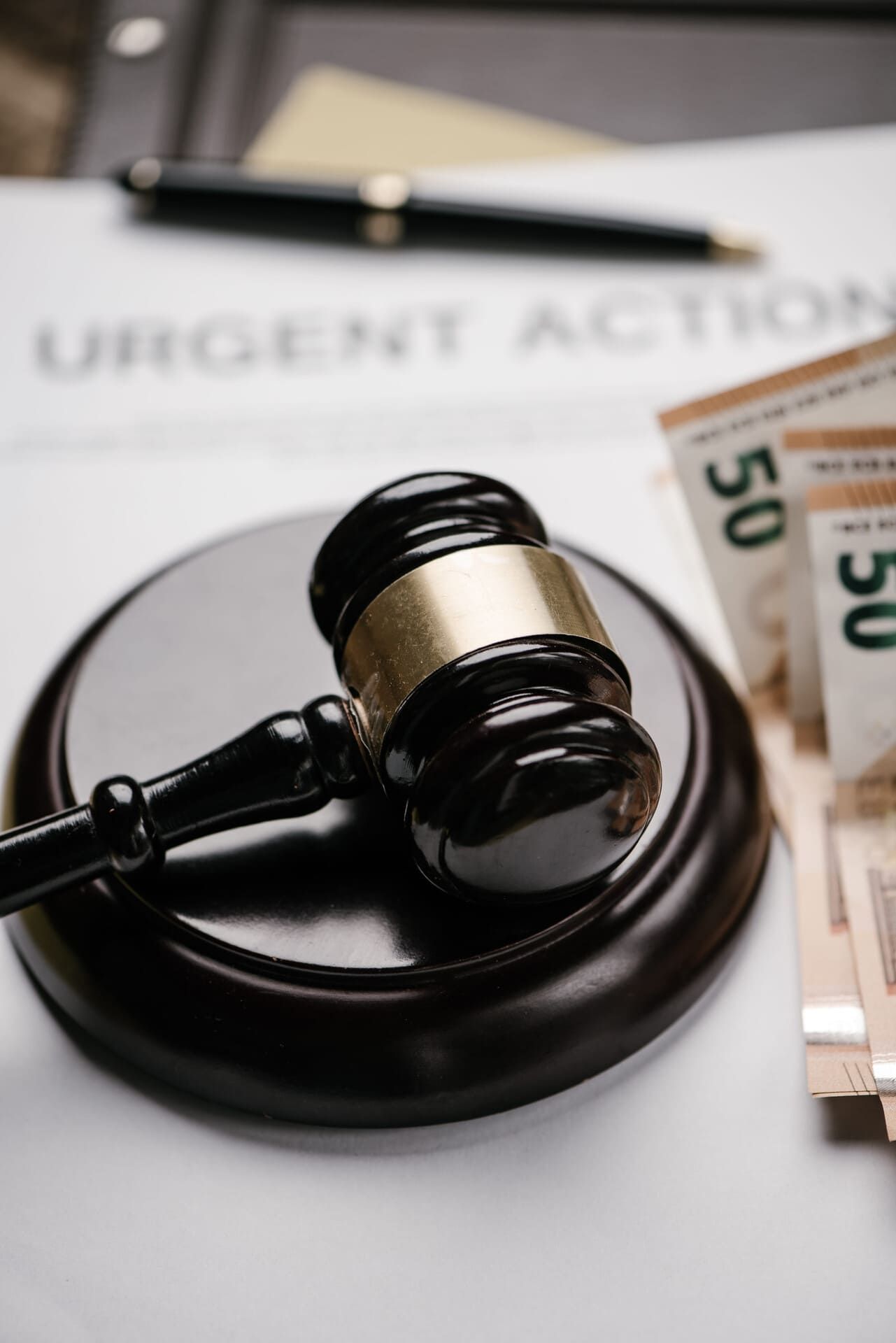 Mazo de abogado sobre documento de acción urgente con billetes apilados.