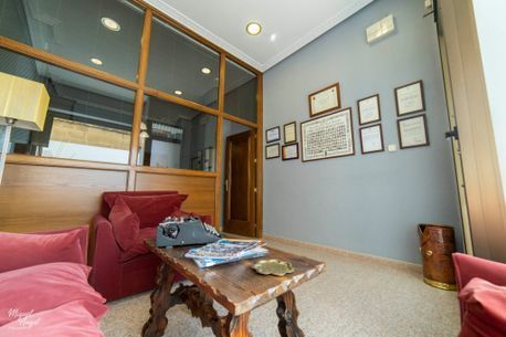 Moderna sala de espera de oficina con sofás rojos, mesa baja, cuadros enmarcados en la pared y mampara de cristal.