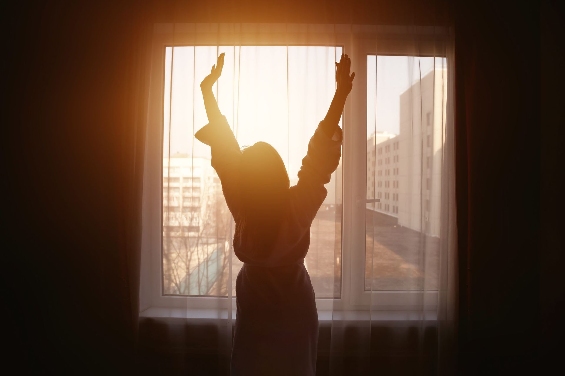  Frau streckt sich vor dem Fenster im Sonnenschein