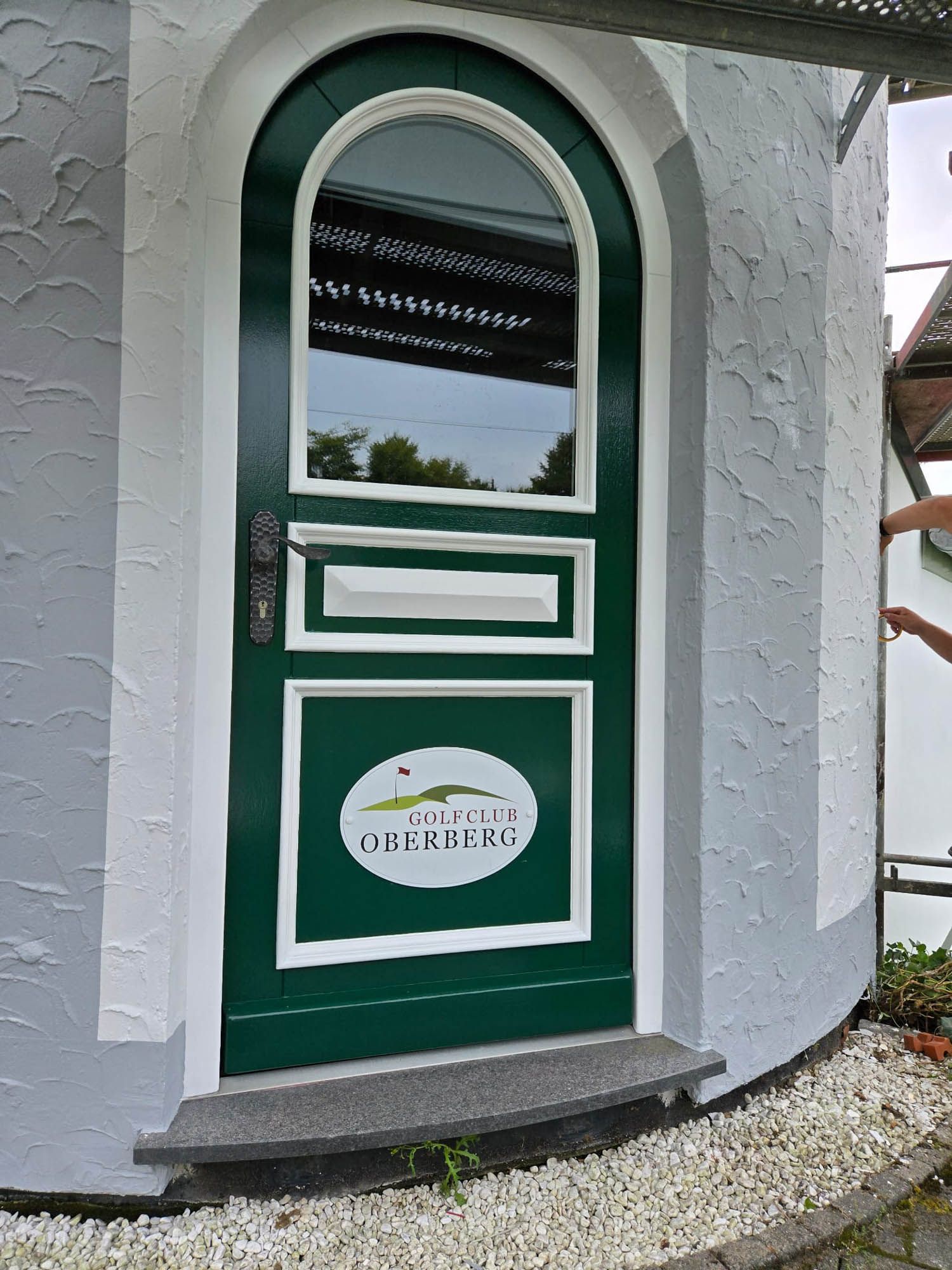 An einem weißen Gebäude befindet sich eine grüne Tür mit weißem Rand.