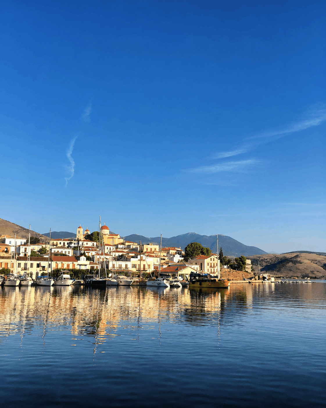 Ηλιόλουστο παραθαλάσσιο χωριό με πολύχρωμα κτίρια που αντανακλώνται σε ήρεμα μπλε νερά κάτω από έναν καθαρό ουρανό