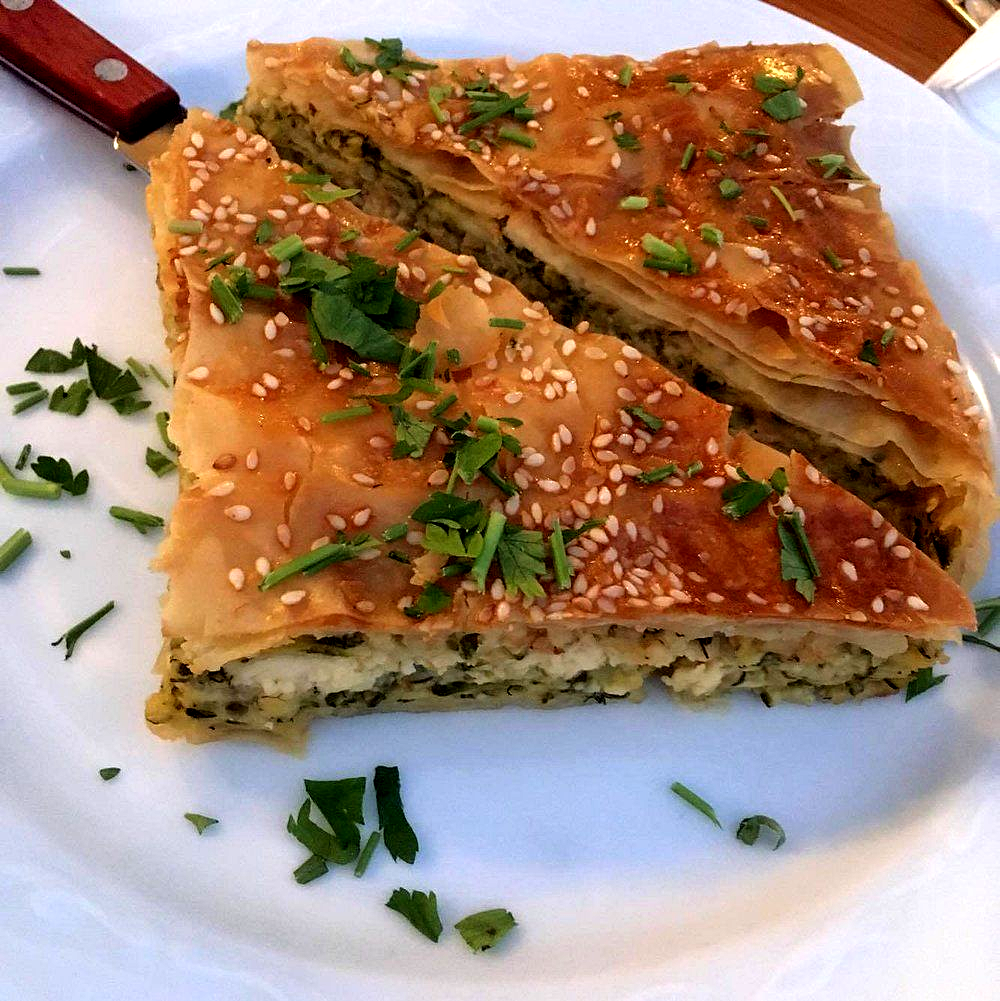 Κόψτε φέτες αλμυρής ζύμης με σουσάμι σε ένα λευκό πιάτο, γαρνιρισμένες με ψιλοκομμένα μυρωδικά.