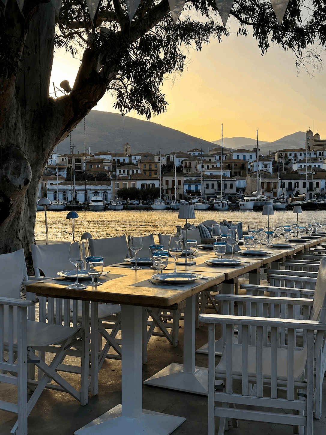 Ηλιόλουστα τραπέζια και καρέκλες εστιατορίου μπροστά στην παραλία με θέα στο λιμάνι κατά το ηλιοβασίλεμα