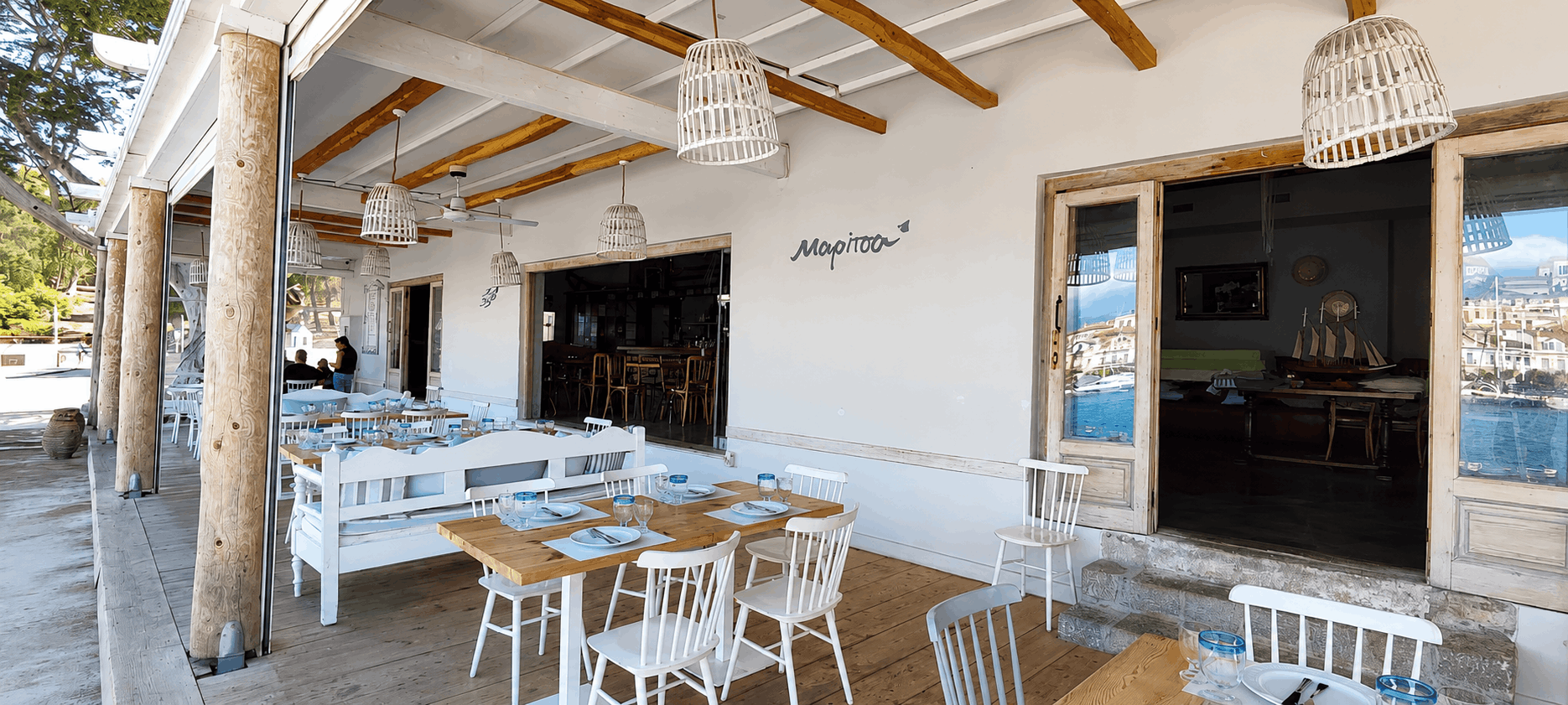 Ρουστίκ βεράντα καφέ με λευκά τραπέζια και καρέκλες κάτω από ξύλινη πέργκολα και κρεμαστά φωτιστικά