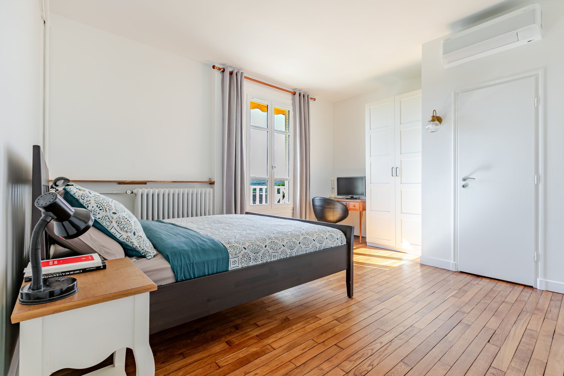 Chambre à coucher avec lit, table de chevet, fenêtre et armoire ; lumière naturelle et plancher en bois.