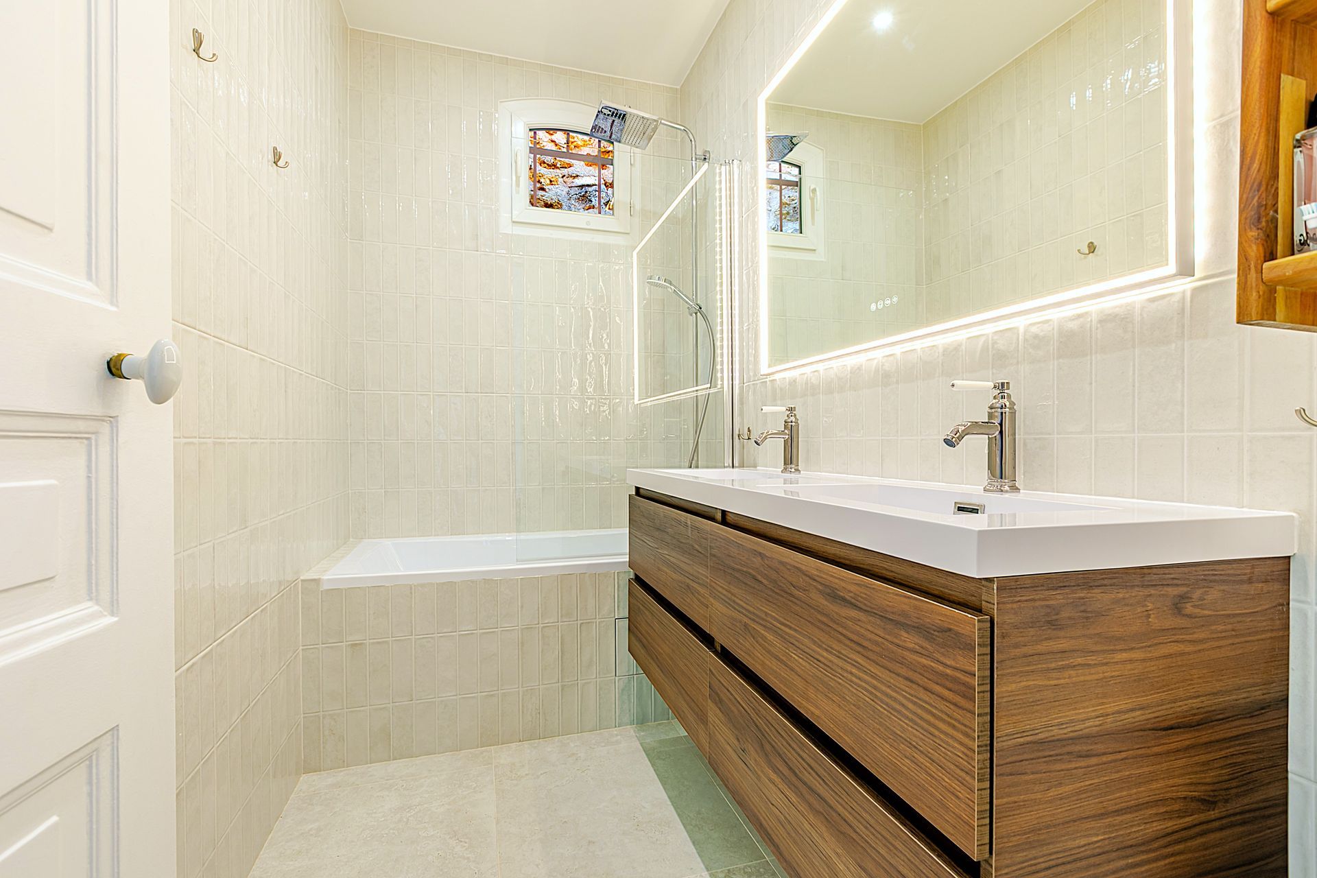 Salle de bain avec vanité en bois, grand miroir, carrelage blanc et baignoire.