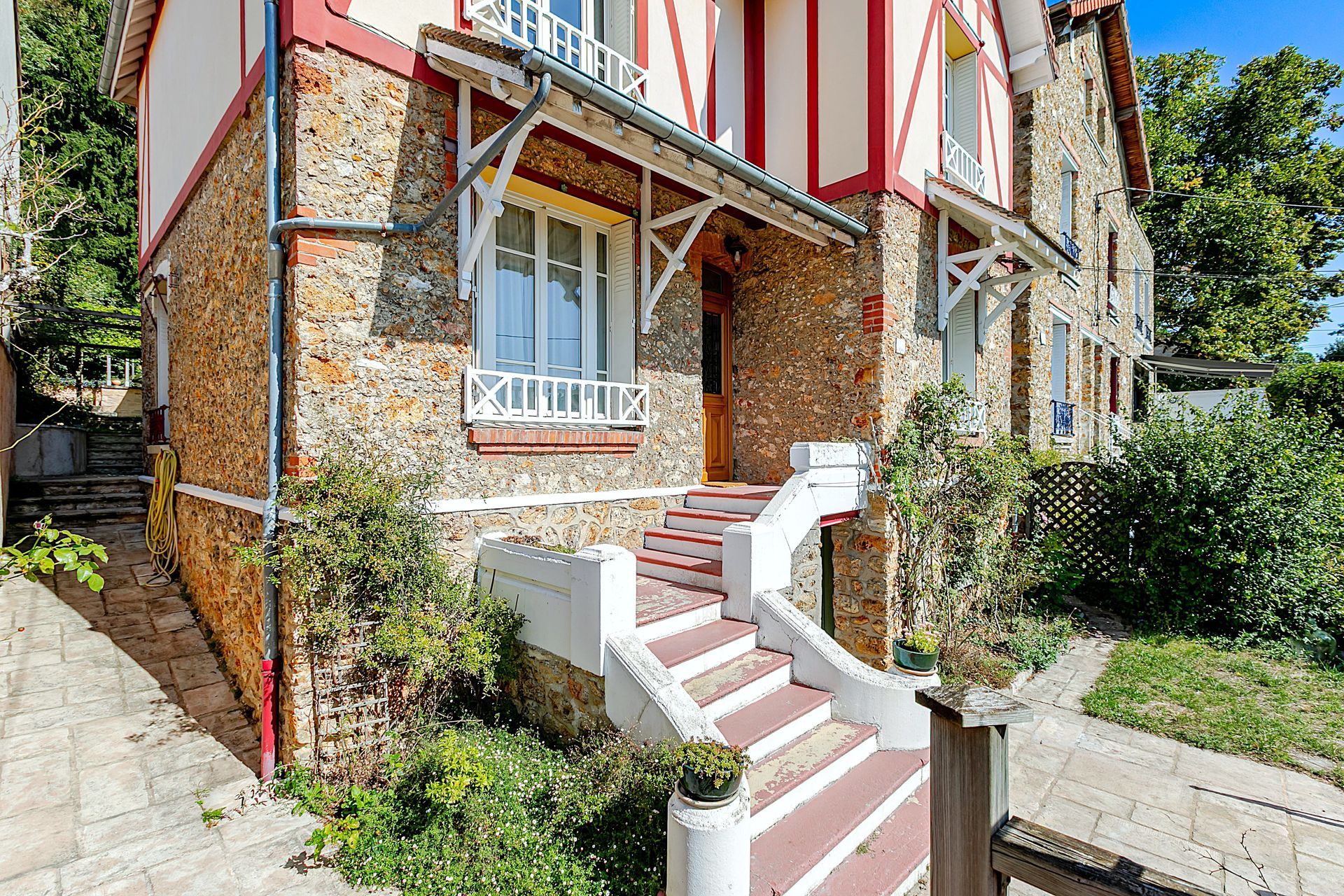 Maison en pierre avec colombages rouges, marches menant à la porte d'entrée et aménagement paysager.