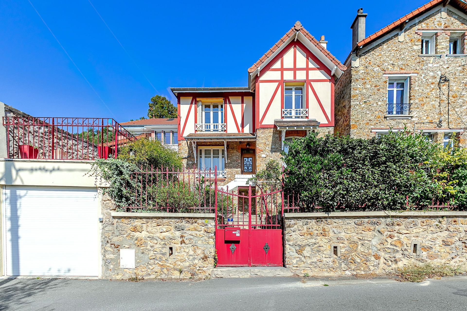 Maison aux colombages rouges, avec portail et mur rouges. Construction en pierre et brique. Ciel bleu éclatant.