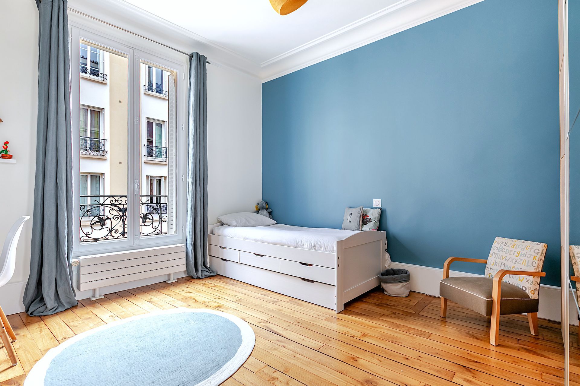 Chambre avec mur d'accent bleu, lit blanc, fenêtre avec rideaux bleus et plancher de bois franc.