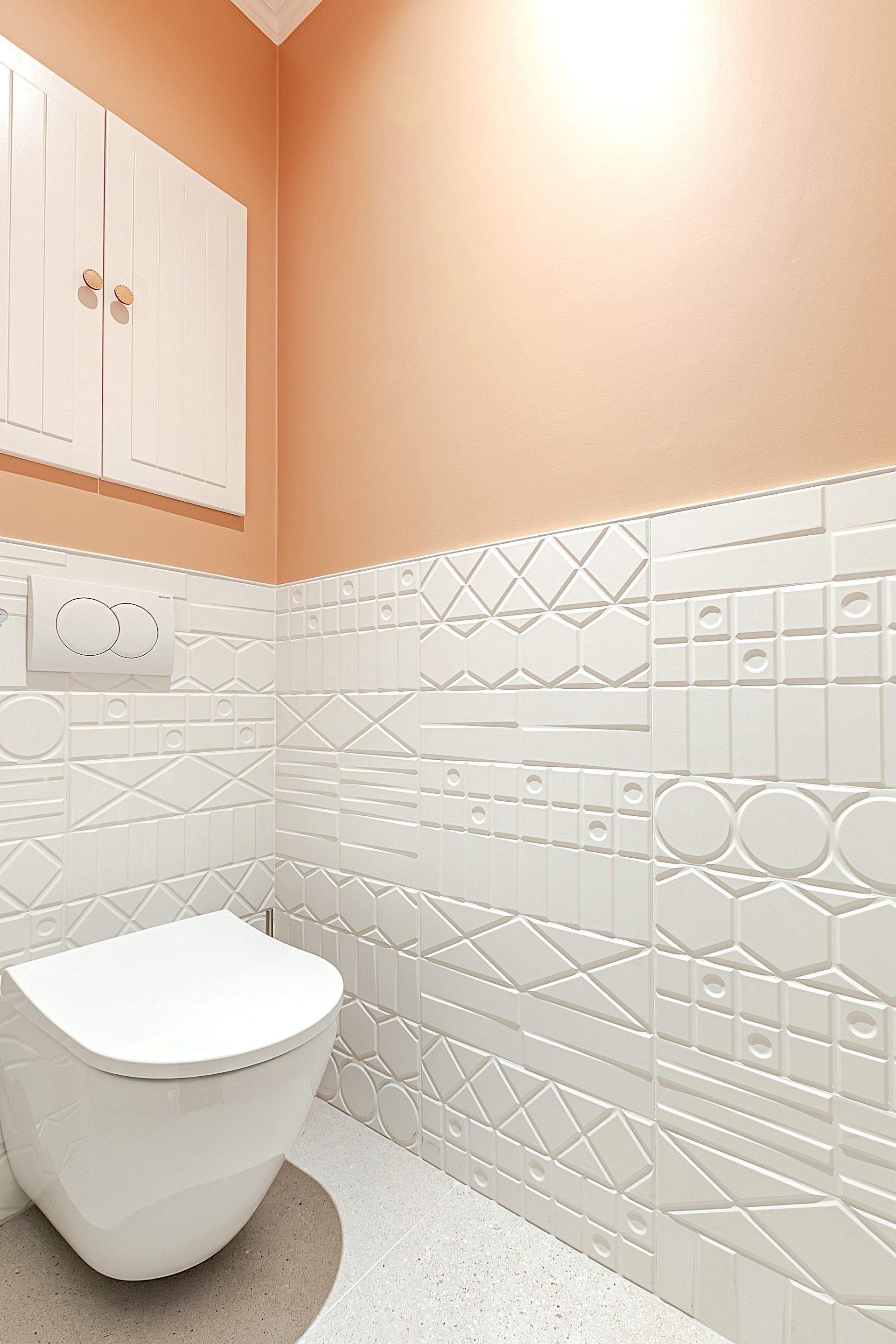 Toilettes blanches dans une petite salle de bains avec carrelage blanc à motifs et murs couleur pêche.