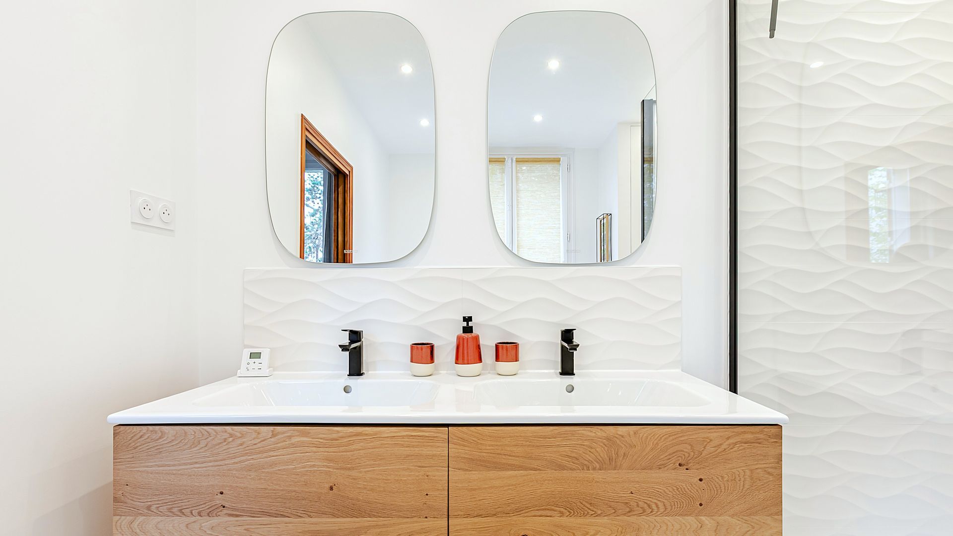 Salle de bains avec deux miroirs ovales au-dessus d'une vanité en bois avec robinets noirs et distributeurs de savon en céramique.