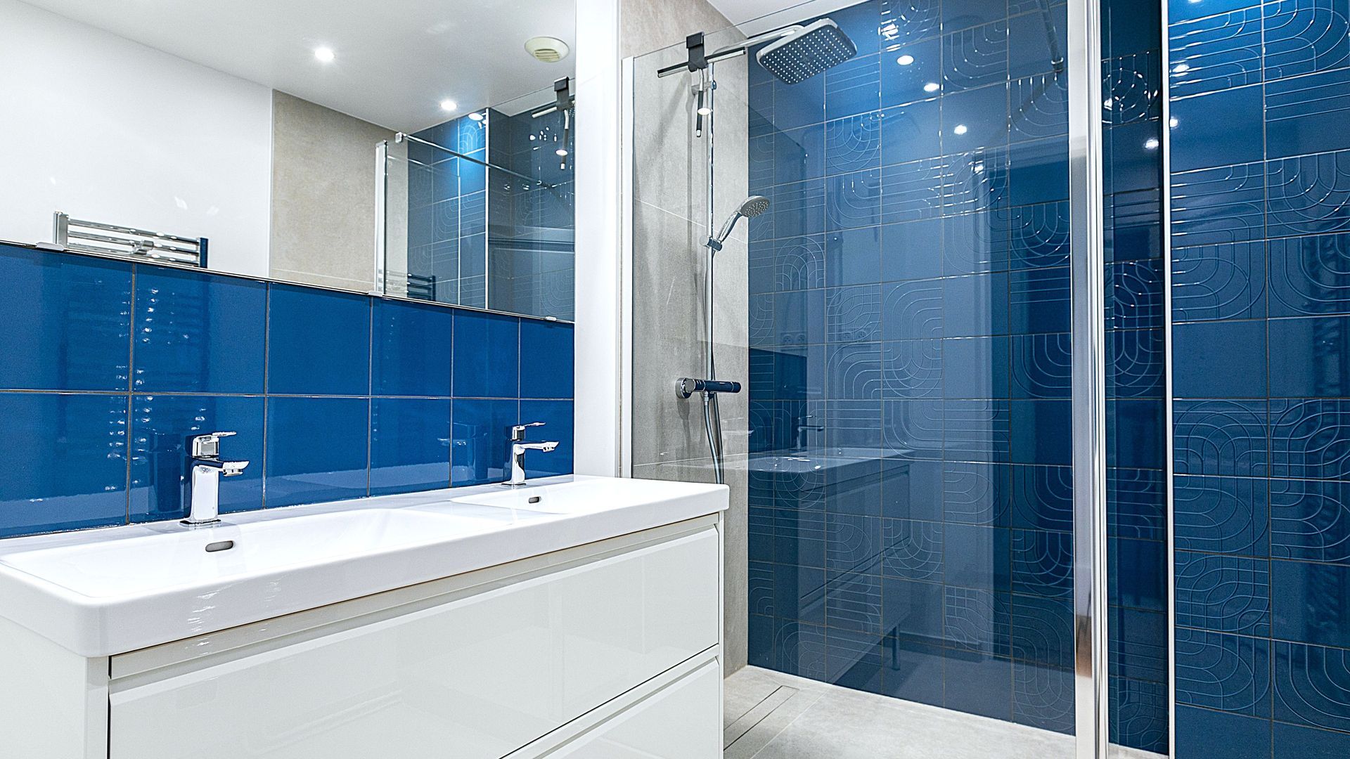 Salle de bains moderne avec vanité blanche, mur carrelé bleu et douche en verre.