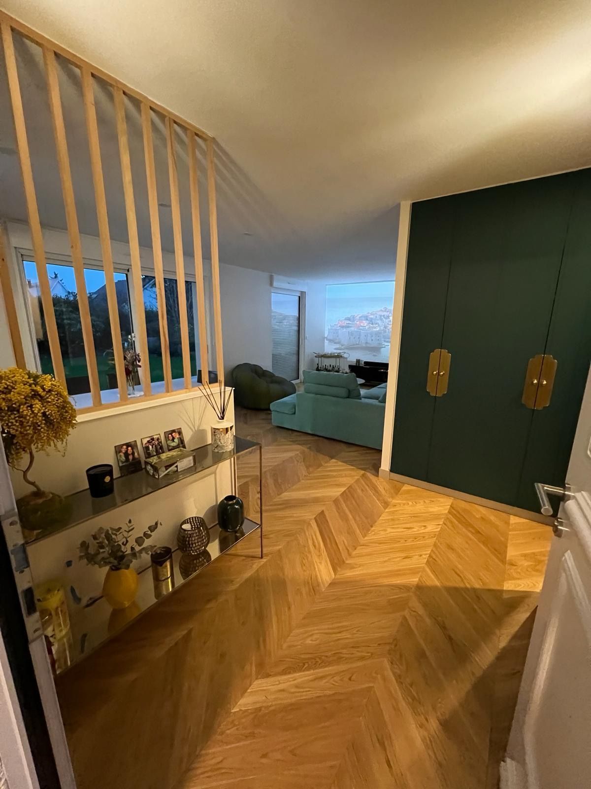 Entrée avec plancher en bois à chevrons, cloison en bois à lattes, mur bleu sarcelle et canapé aqua.