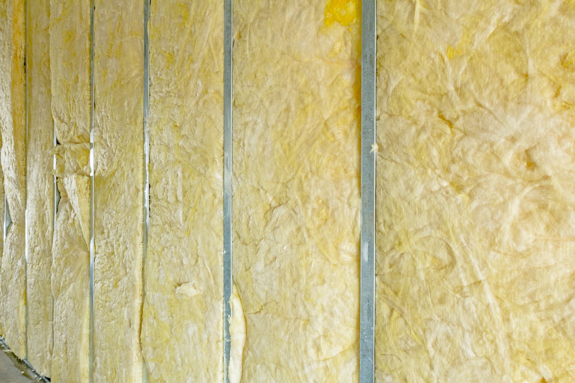 Isolant installé dans une cavité murale entre des montants métalliques ; matériau jaune et blanc cassé.