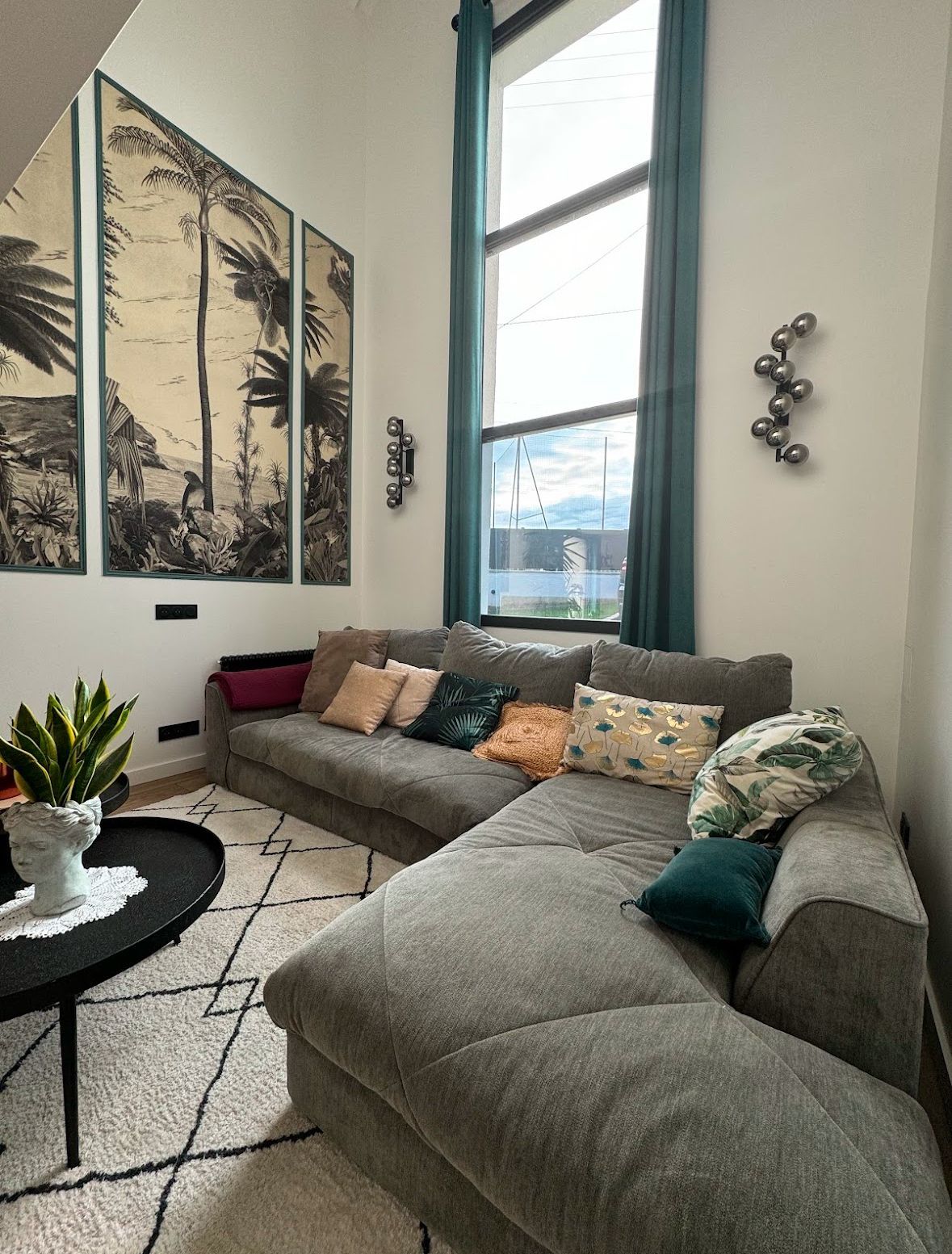 Salon avec canapé sectionnel gris, grande fenêtre, œuvres d'art et table basse noire.