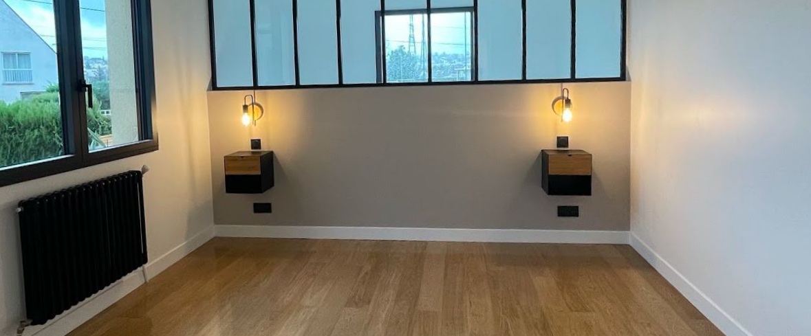 Une chambre avec un mur clair et un parquet. Deux tables de chevet flottantes encadrent une fenêtre.