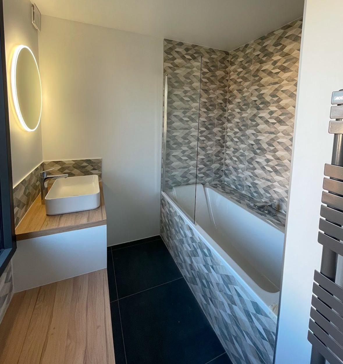 Petite salle de bains avec baignoire, lavabo et carrelage noir au sol ; carrelage mural à motifs.