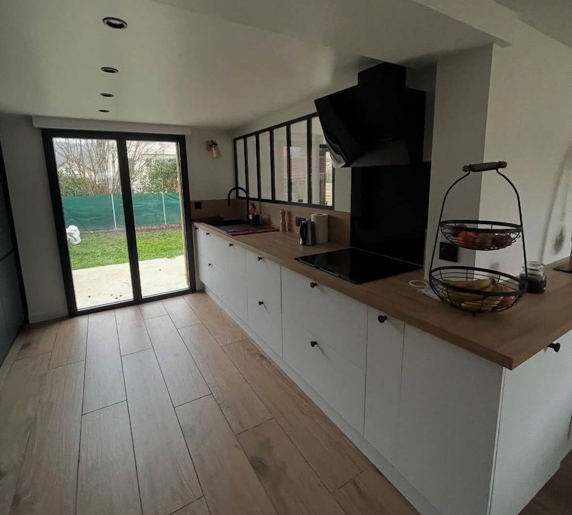 Cuisine moderne avec armoires blanches, comptoirs en bois et appareils électroménagers noirs, avec vue sur la cour arrière.