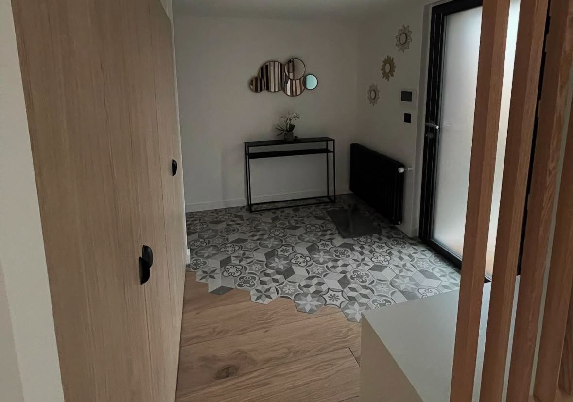 Entrée avec plancher en bois clair, carrelage en mosaïque, console, placard et porte vitrée.