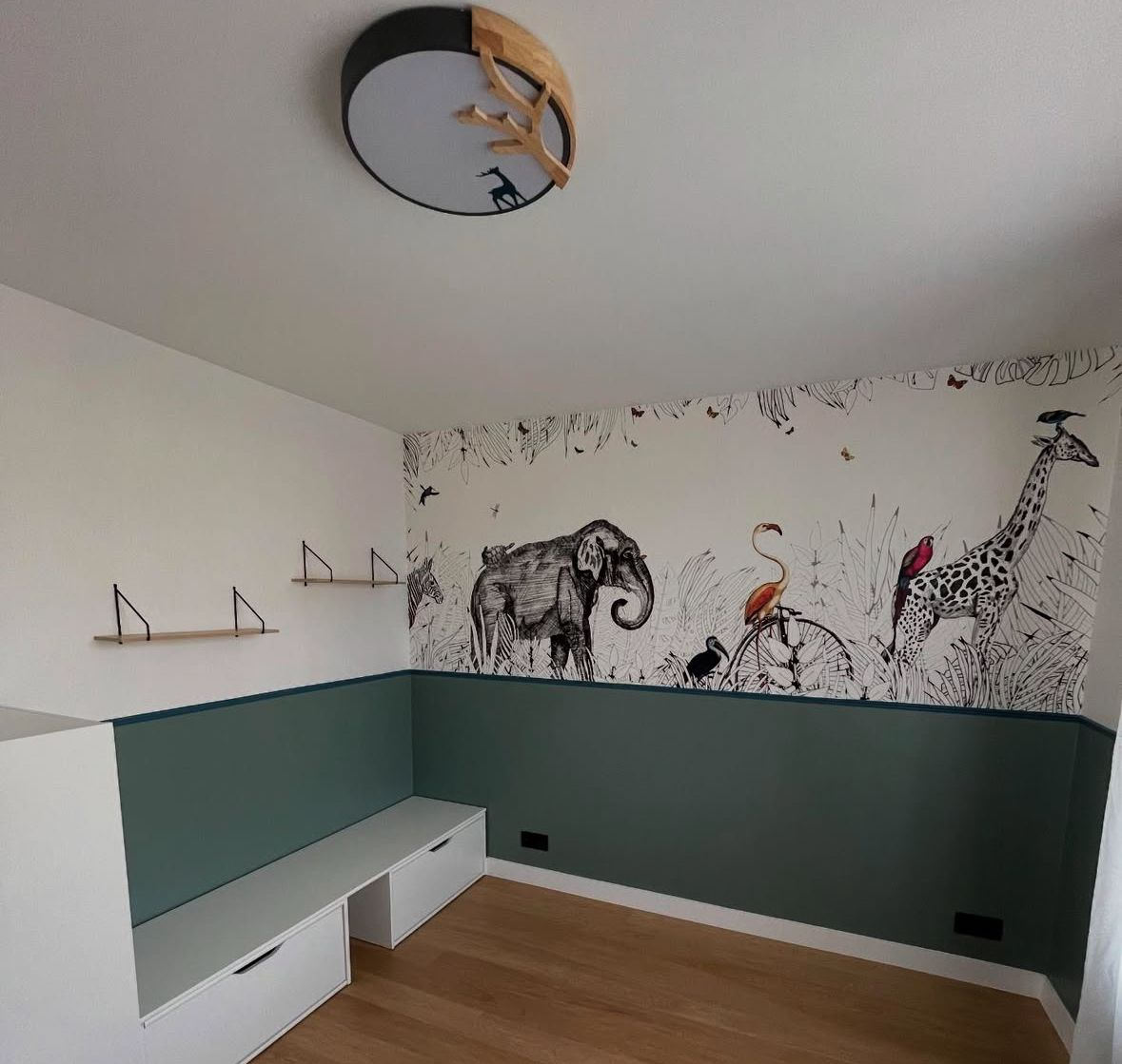 Chambre d'enfant avec fresque animalière. Murs blancs et verts, étagères en bois et luminaire.
