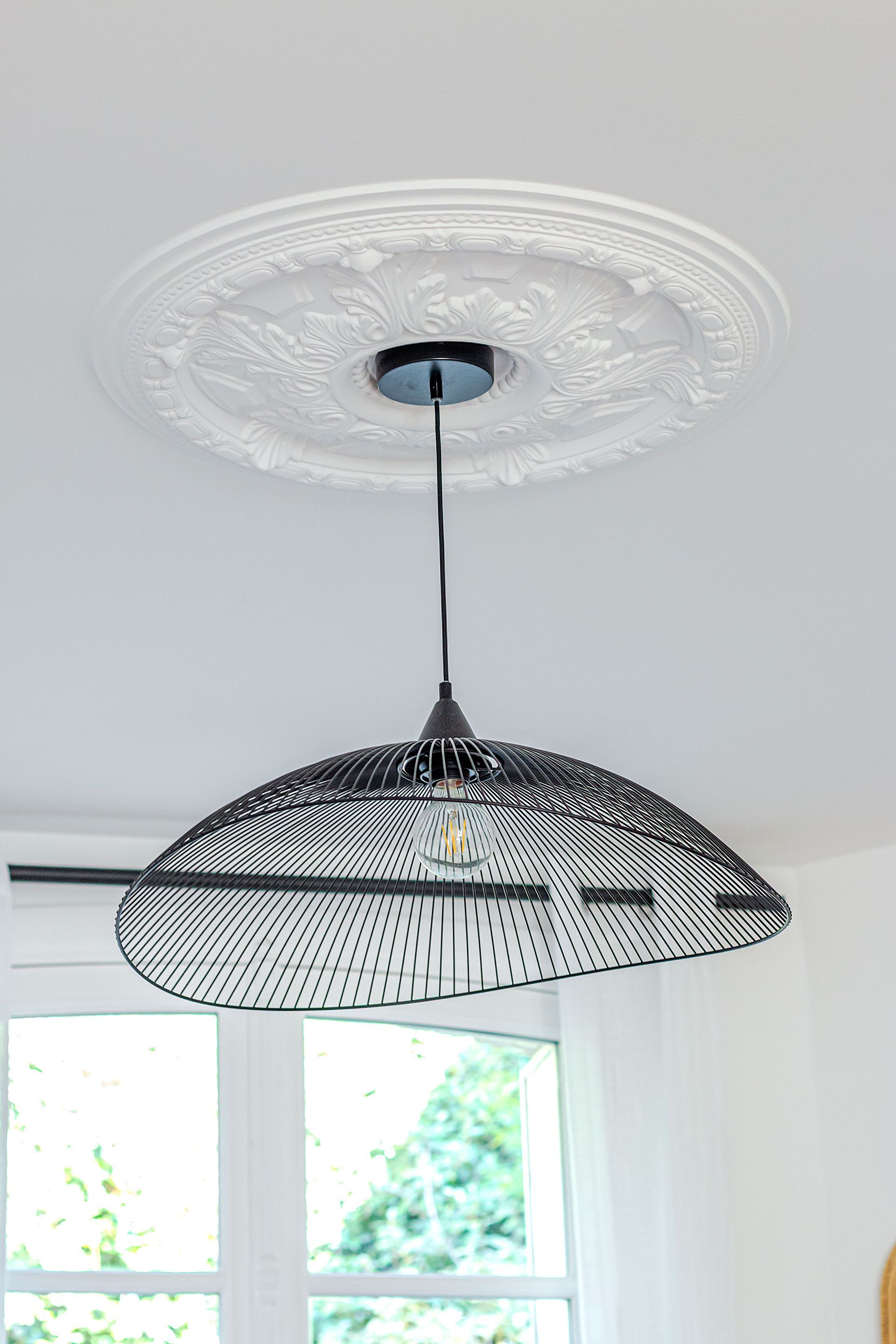 Lampe en fil noir suspendue à un médaillon de plafond décoratif au-dessus d'une fenêtre.