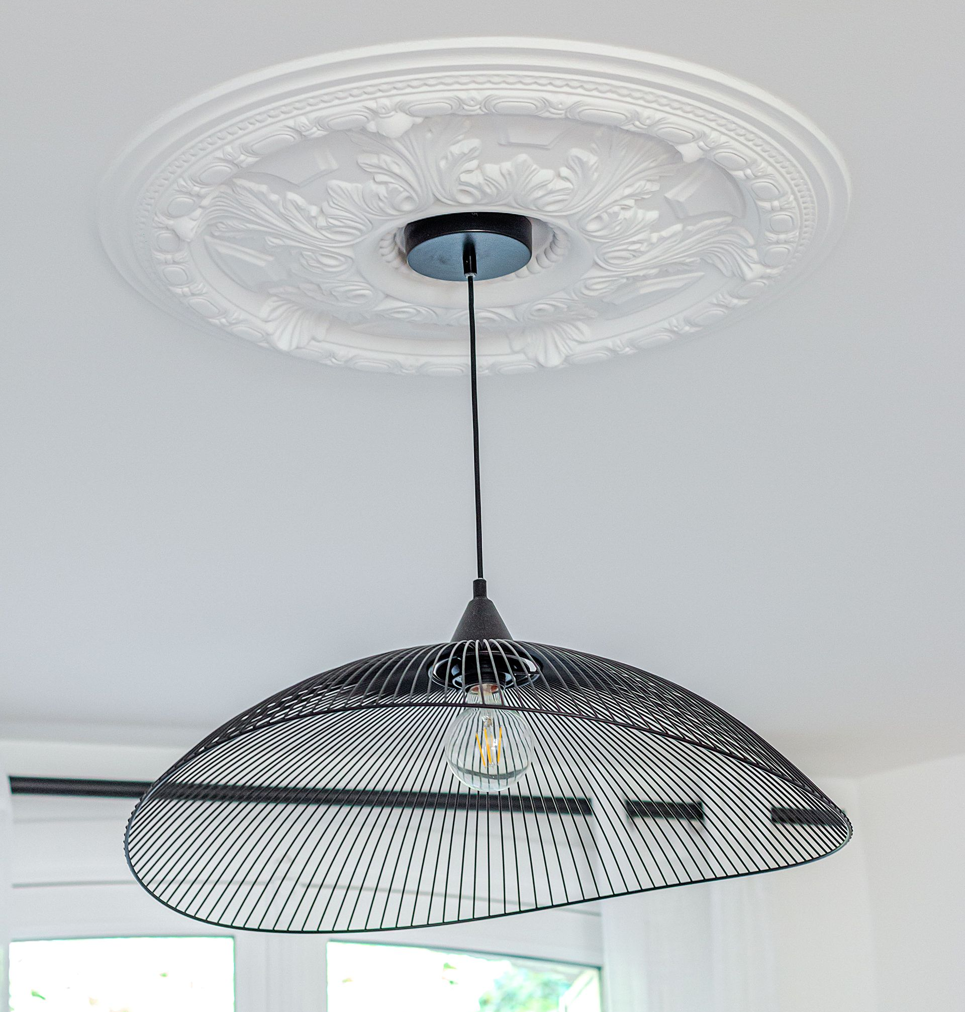Suspension en fil de fer noir sur un plafond blanc avec un médaillon décoratif en plâtre.
