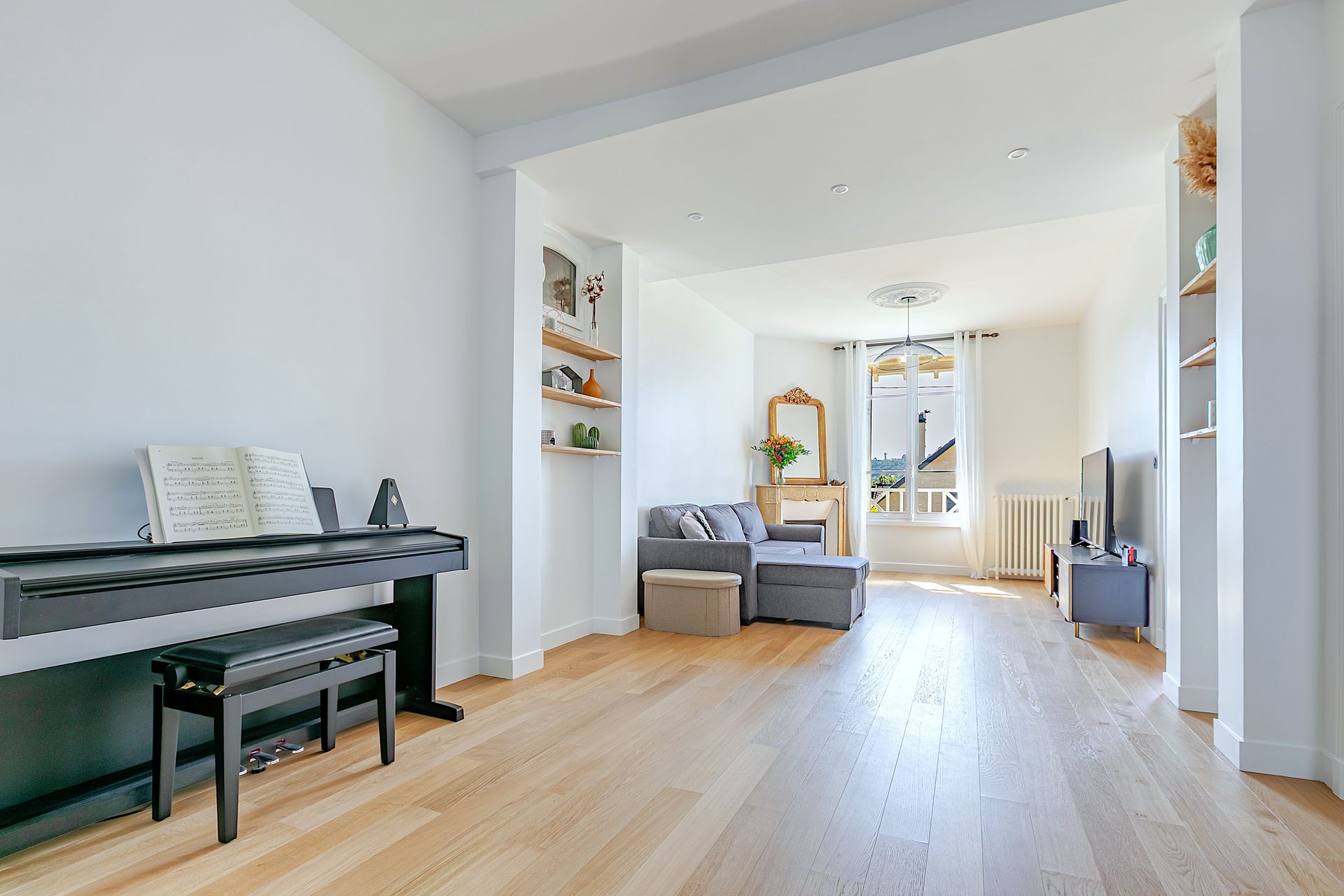 Séjour spacieux et lumineux avec piano, coin salon et parquet.