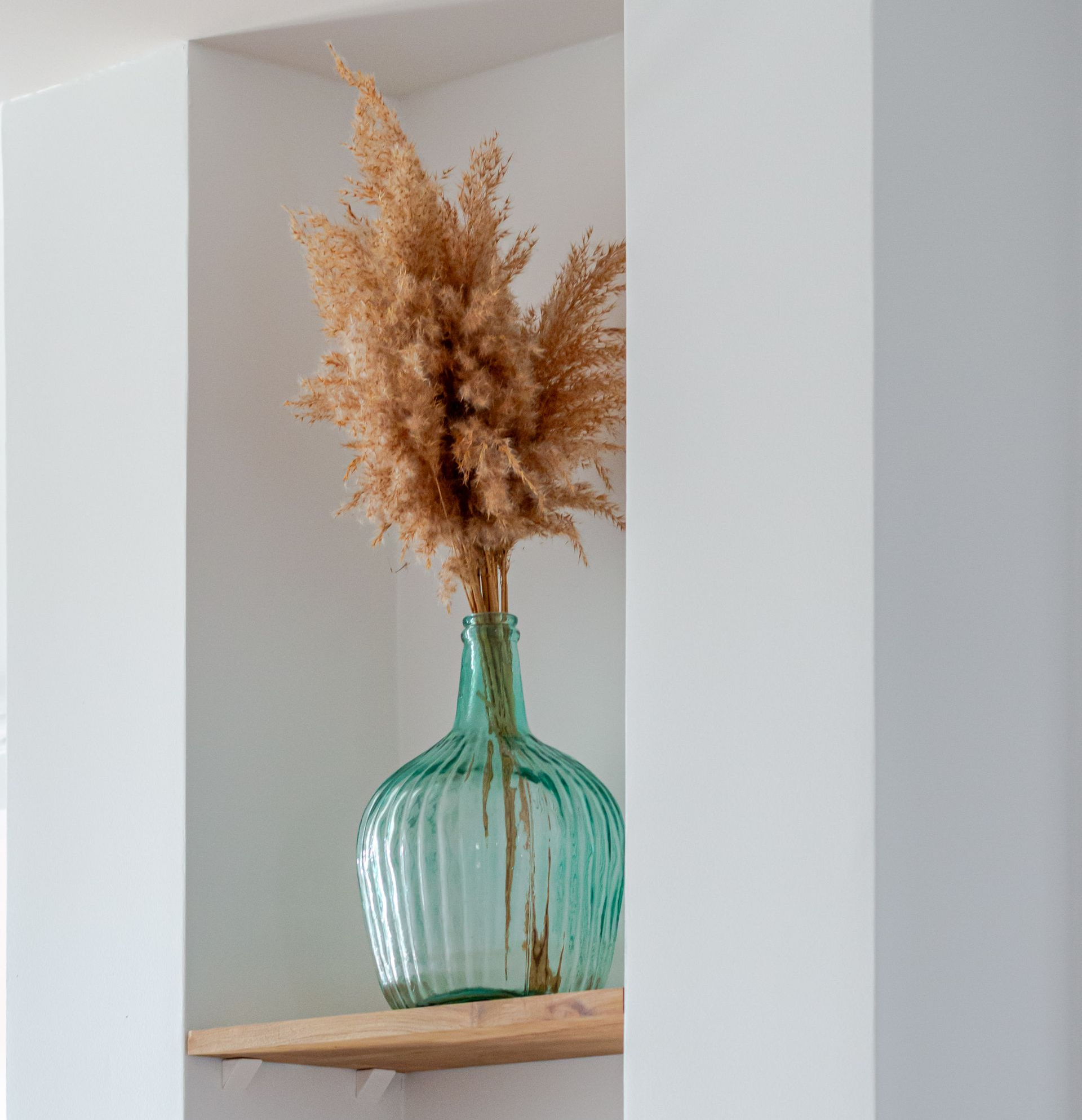 Étagères avec objets décoratifs : fleurs de coton séchées, vase orange, objet en forme de maison, cactus.
