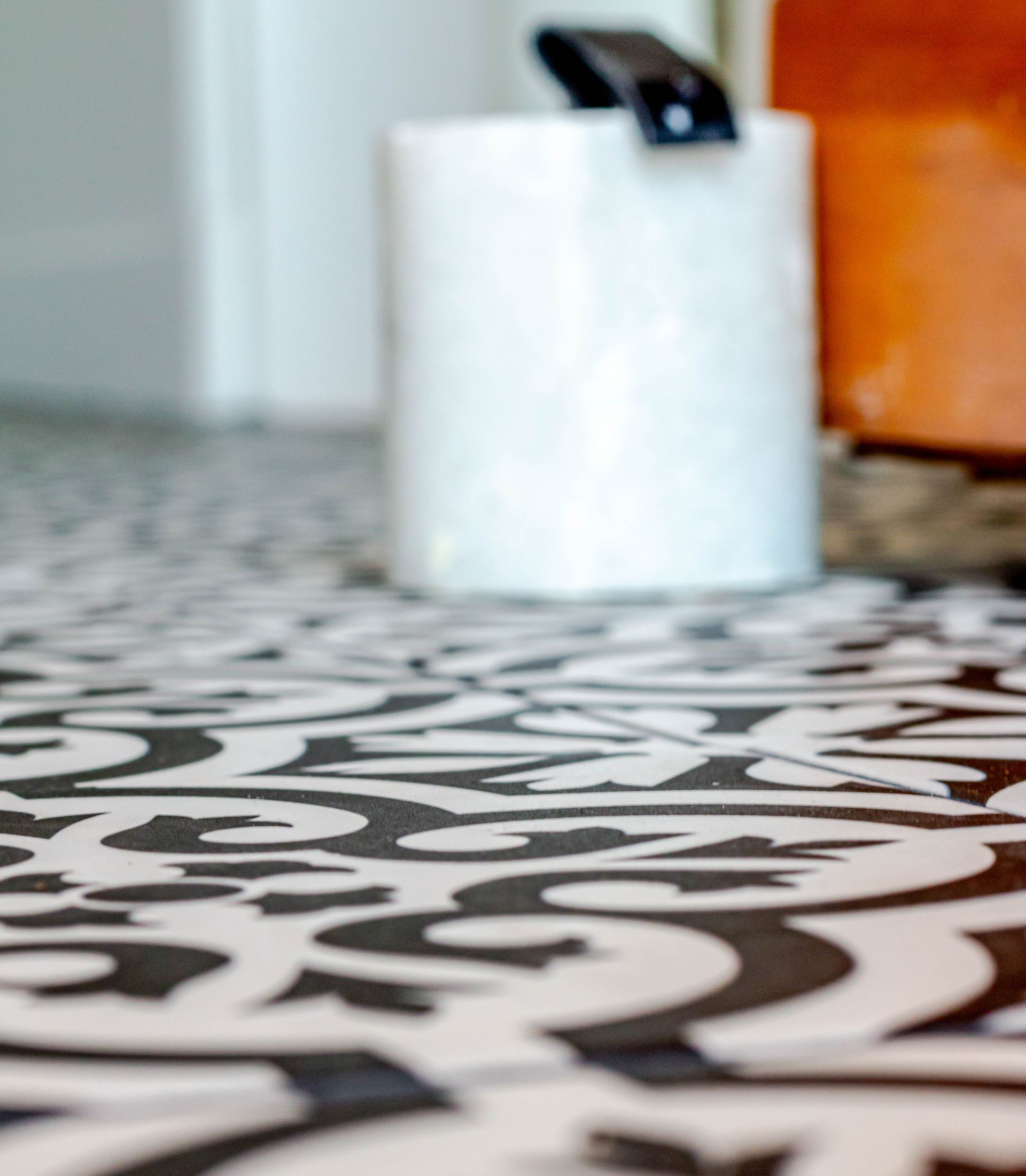 Sol à motifs noirs et blancs avec une bougie blanche et un objet orange en arrière-plan.