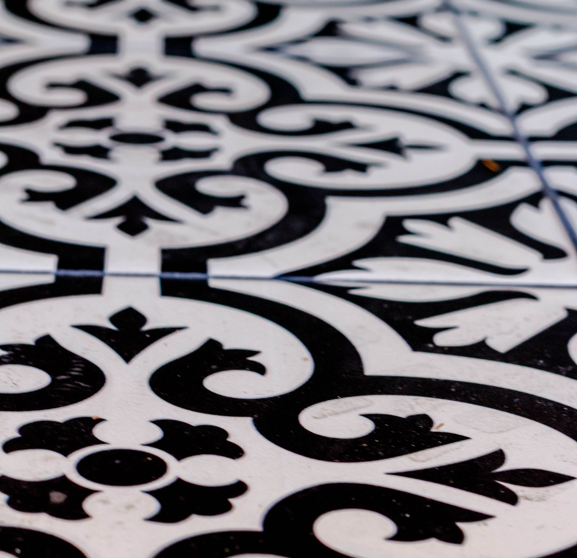 Sol en carrelage à motifs noirs et blancs avec des motifs floraux et de volutes.