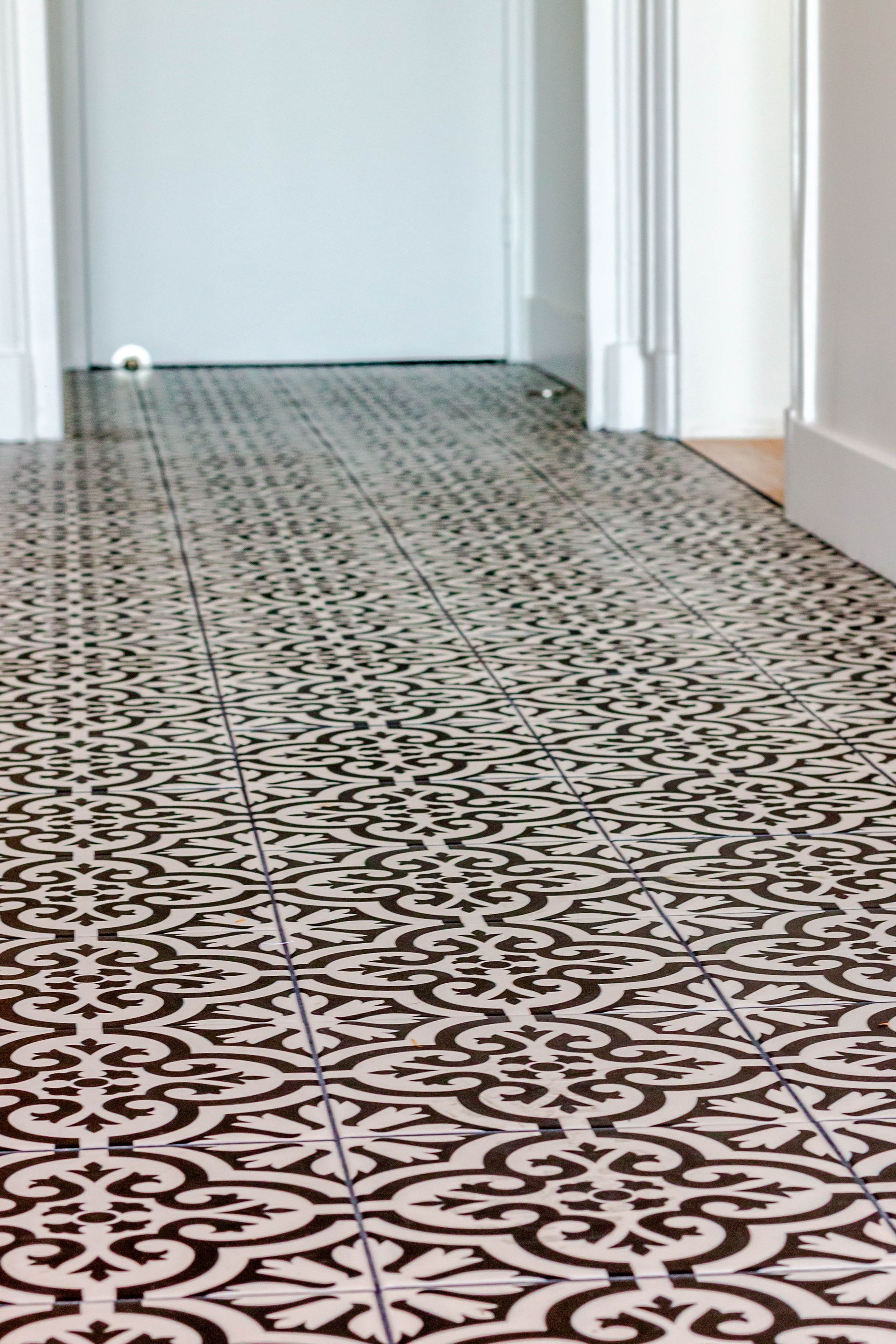 Sol carrelé à motifs noirs et blancs dans un couloir, menant à une porte et des murs de couleur claire.