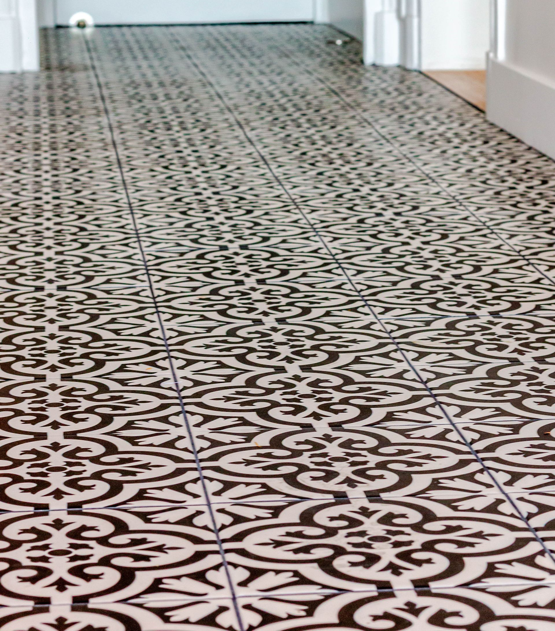 Carrelage à motifs noirs et blancs sur le sol d'un couloir, menant à une porte.