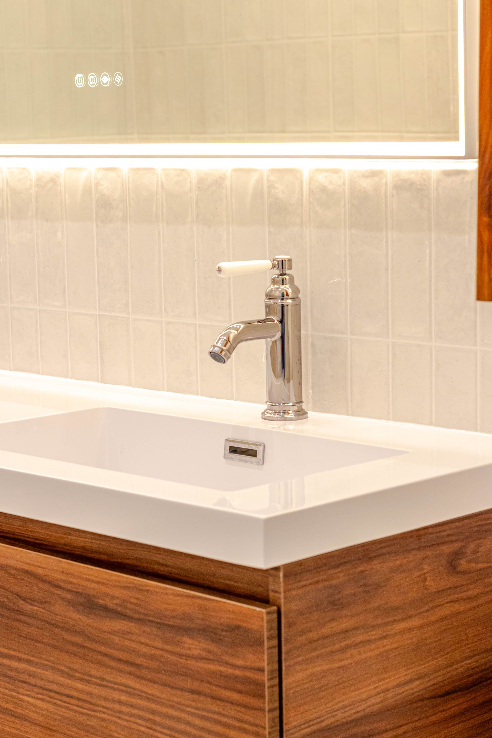 Lavabo de salle de bains blanc avec robinet argenté, armoire marron et dosseret carrelé carré.