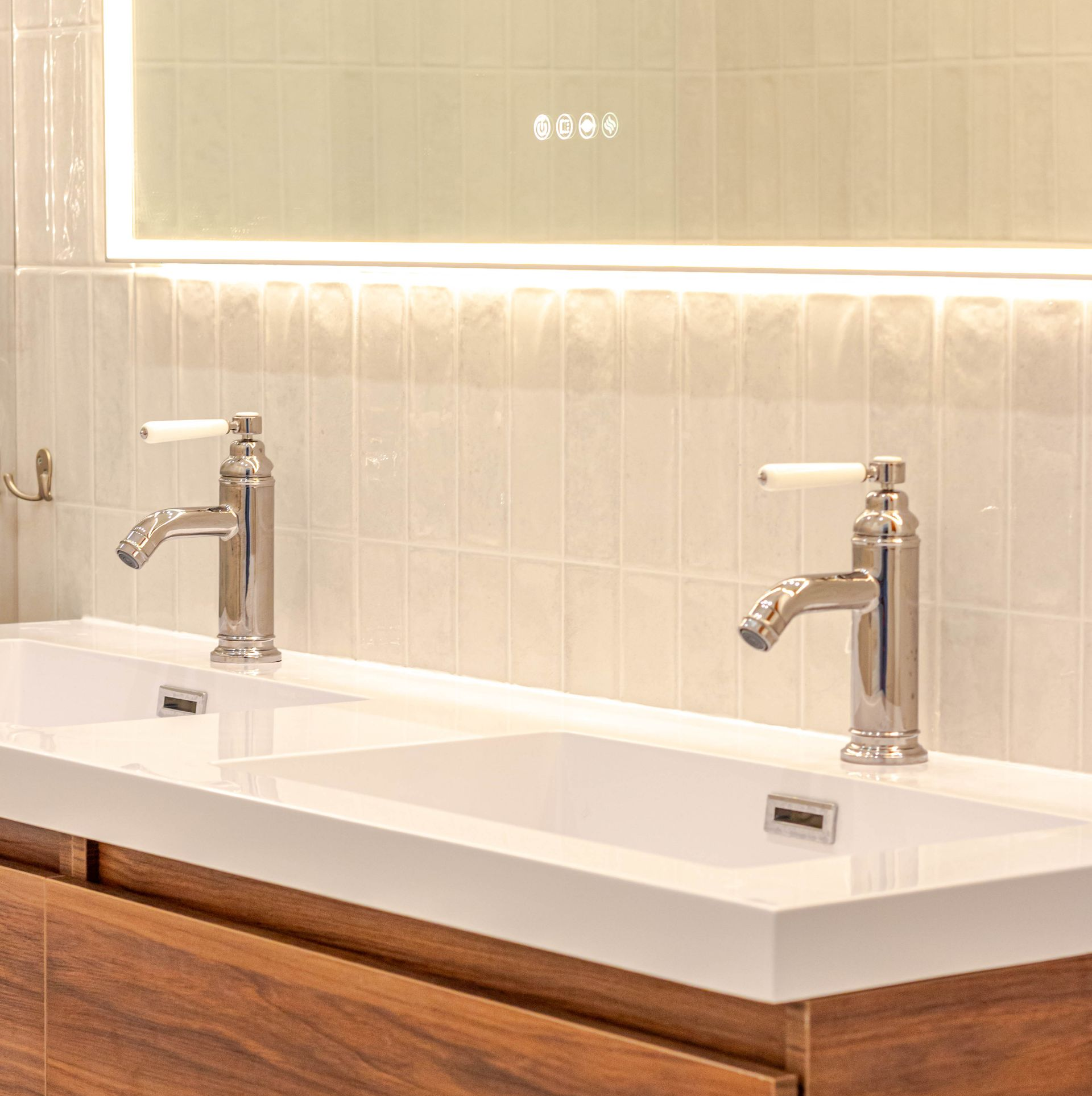 Deux lavabos avec robinets chromés dans une salle de bains moderne, sous un miroir rétroéclairé.