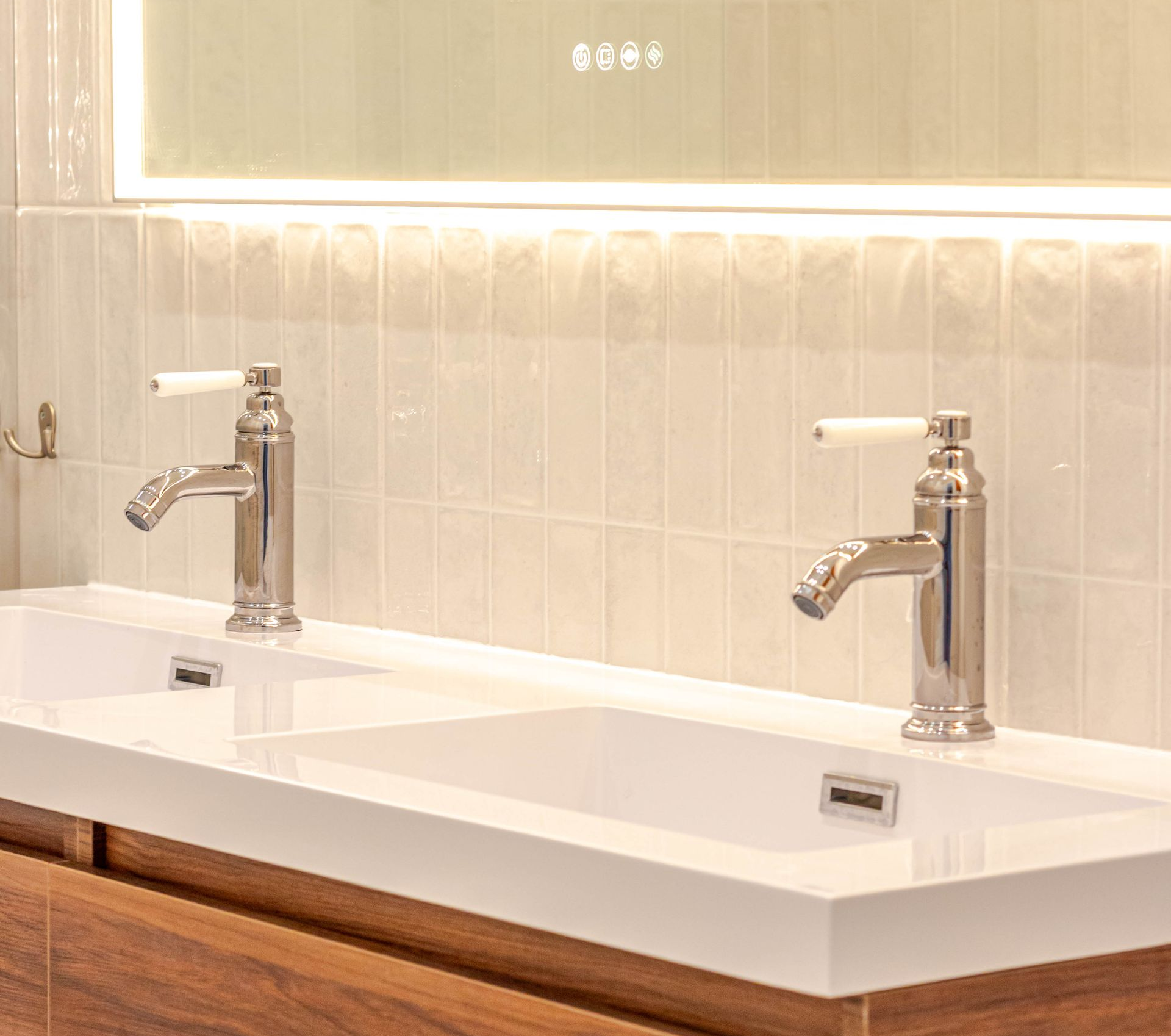 Deux robinets chromés sur un double lavabo blanc, sur un fond de carrelage crème.