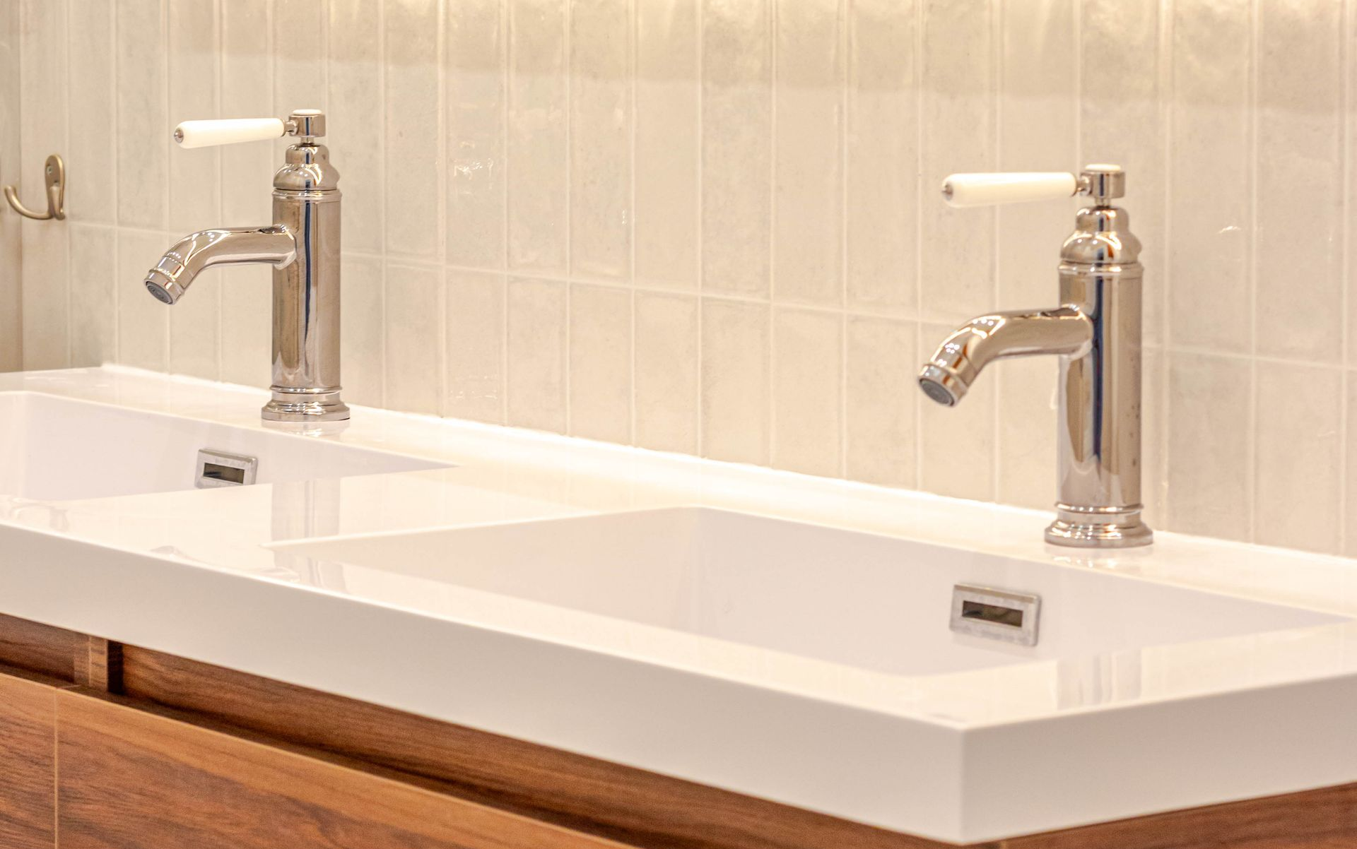 Deux robinets chromés avec poignées blanches au-dessus d'un lavabo blanc, dans une salle de bains.