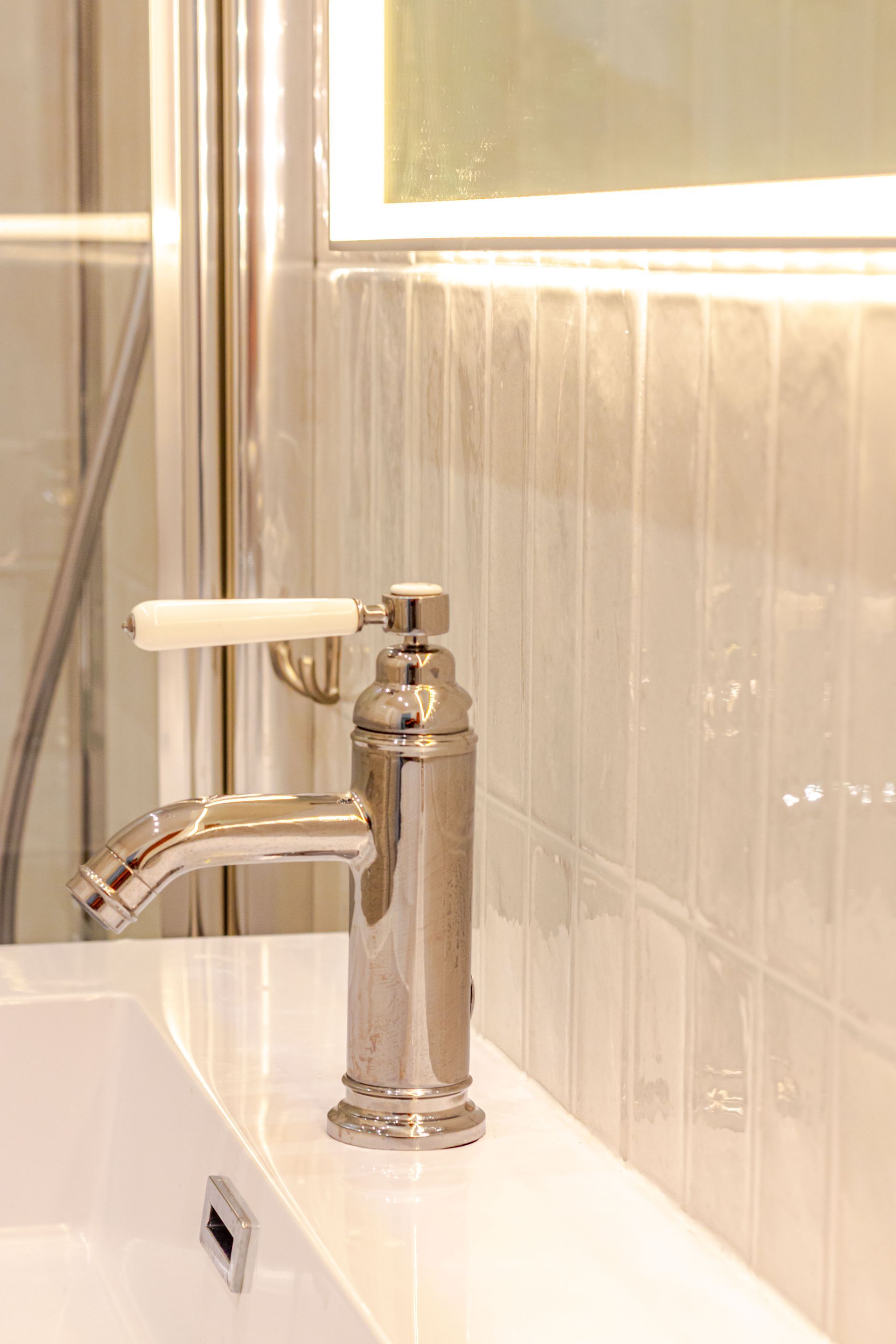 Robinet chromé avec poignée blanche sur un lavabo blanc dans une salle de bains avec carrelage blanc.