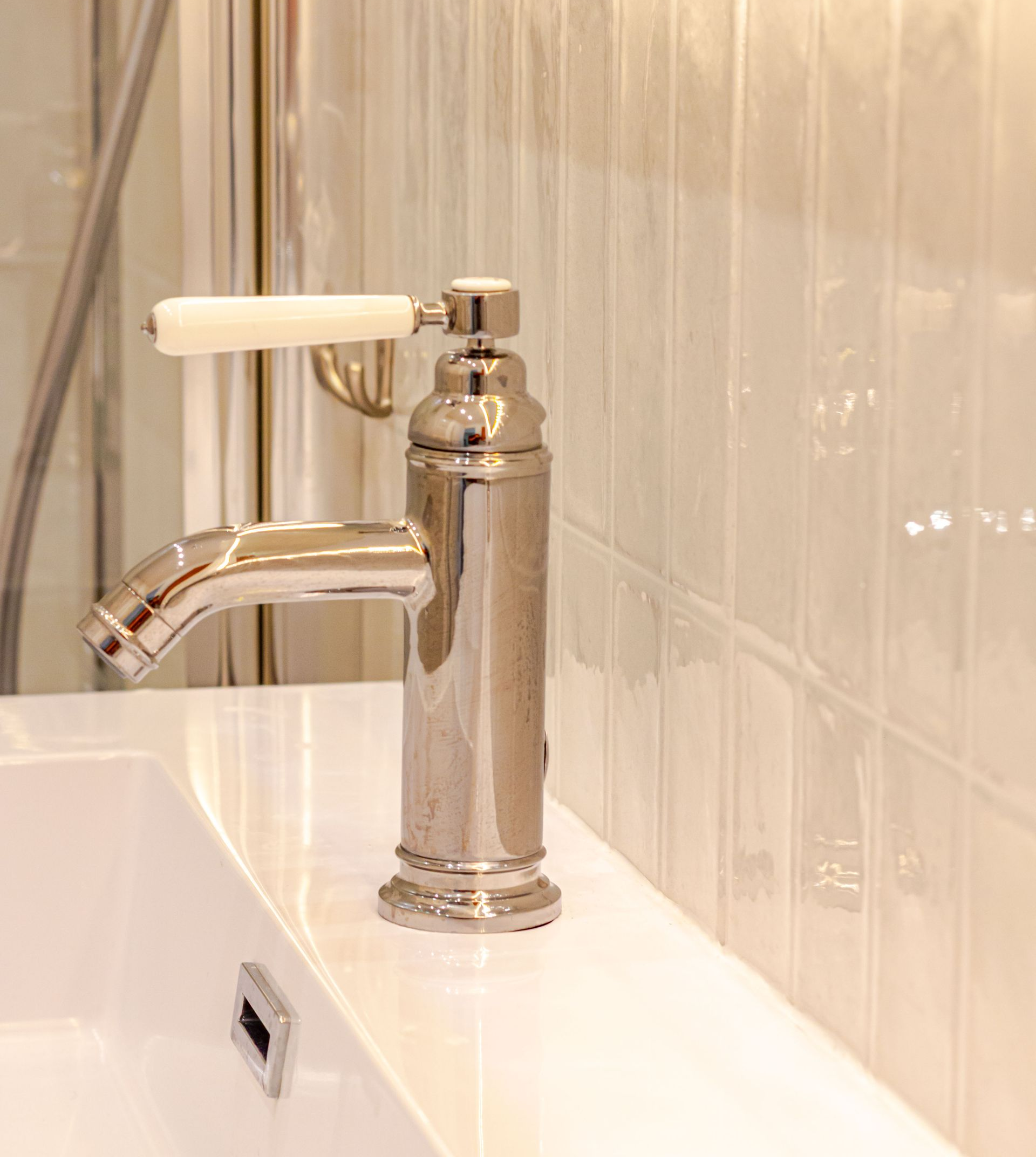 Robinet argenté avec poignée blanche sur un évier blanc sur fond de carrelage blanc.