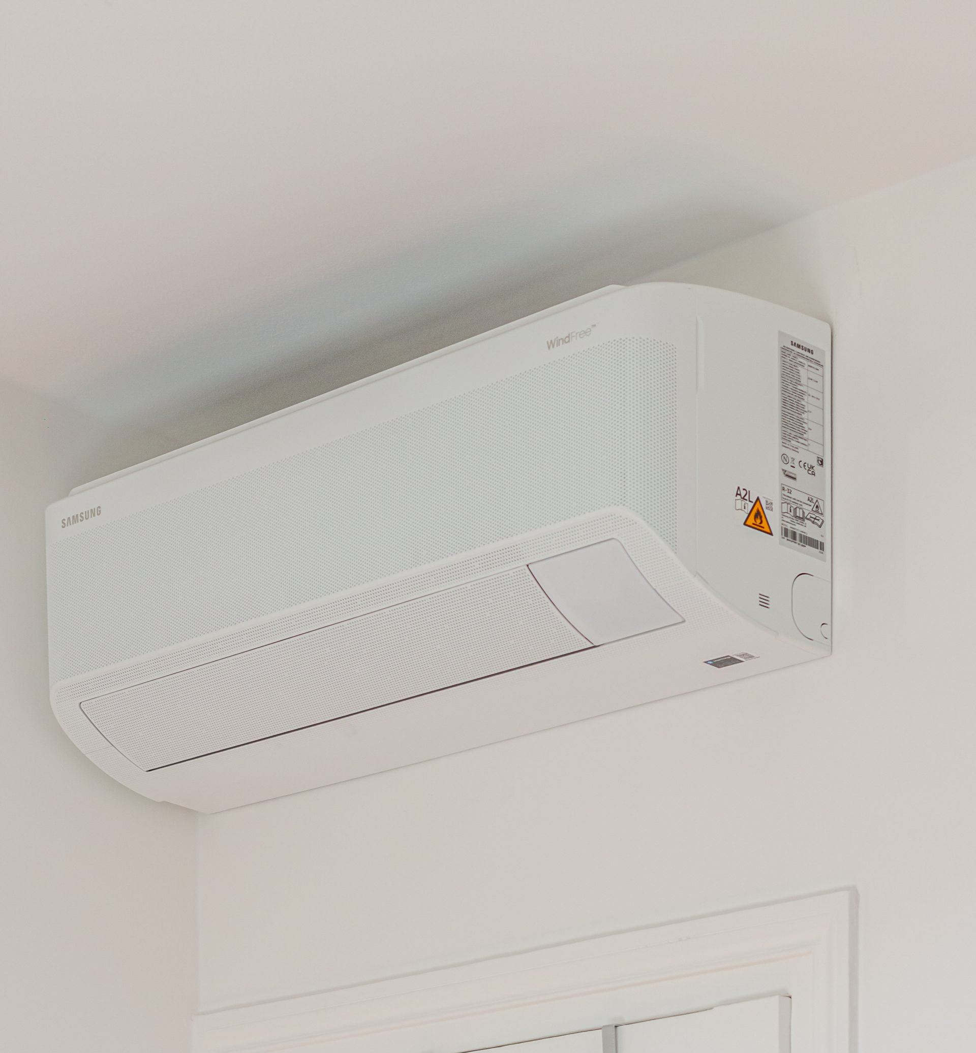 Climatiseur mural blanc sur un mur blanc près d'une fenêtre.