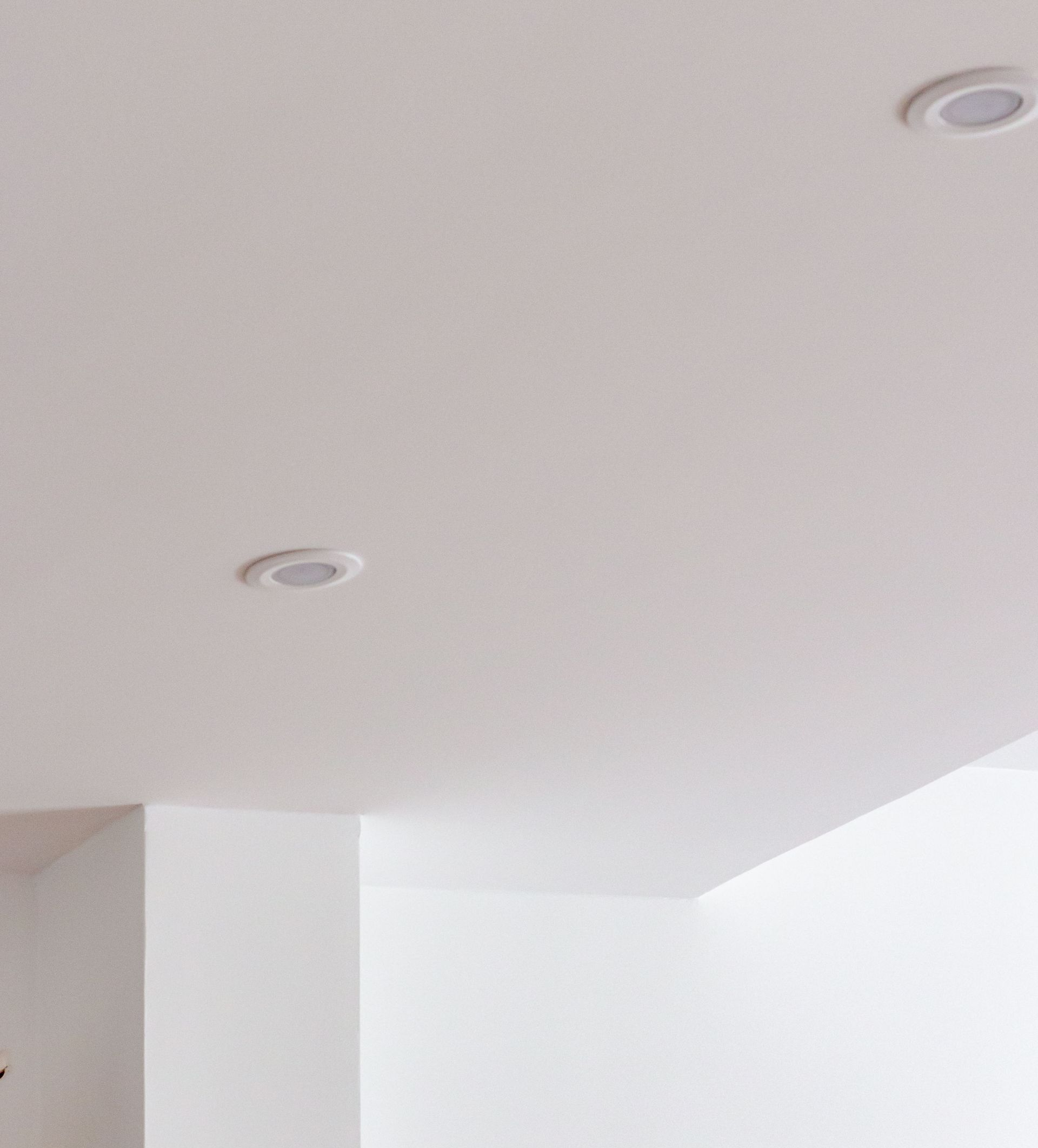 Plafond blanc avec éclairage encastré, un coin de murs blancs dans une pièce.