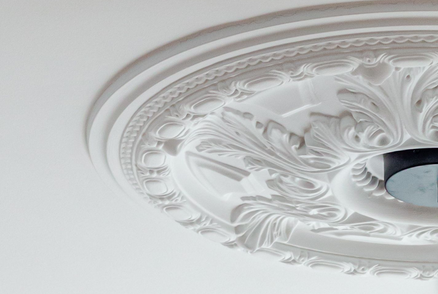 Médaillon de plafond blanc orné de détails floraux et de volutes.