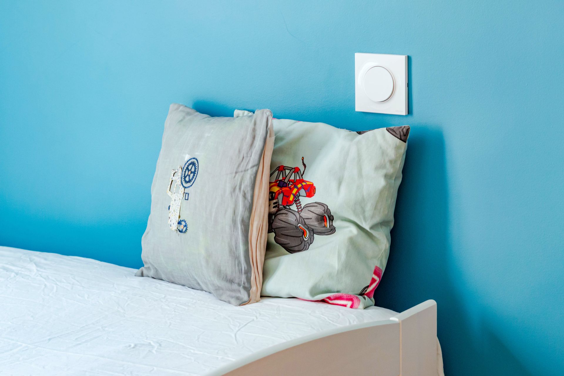 Deux oreillers sur un lit contre un mur bleu, avec un interrupteur au-dessus.